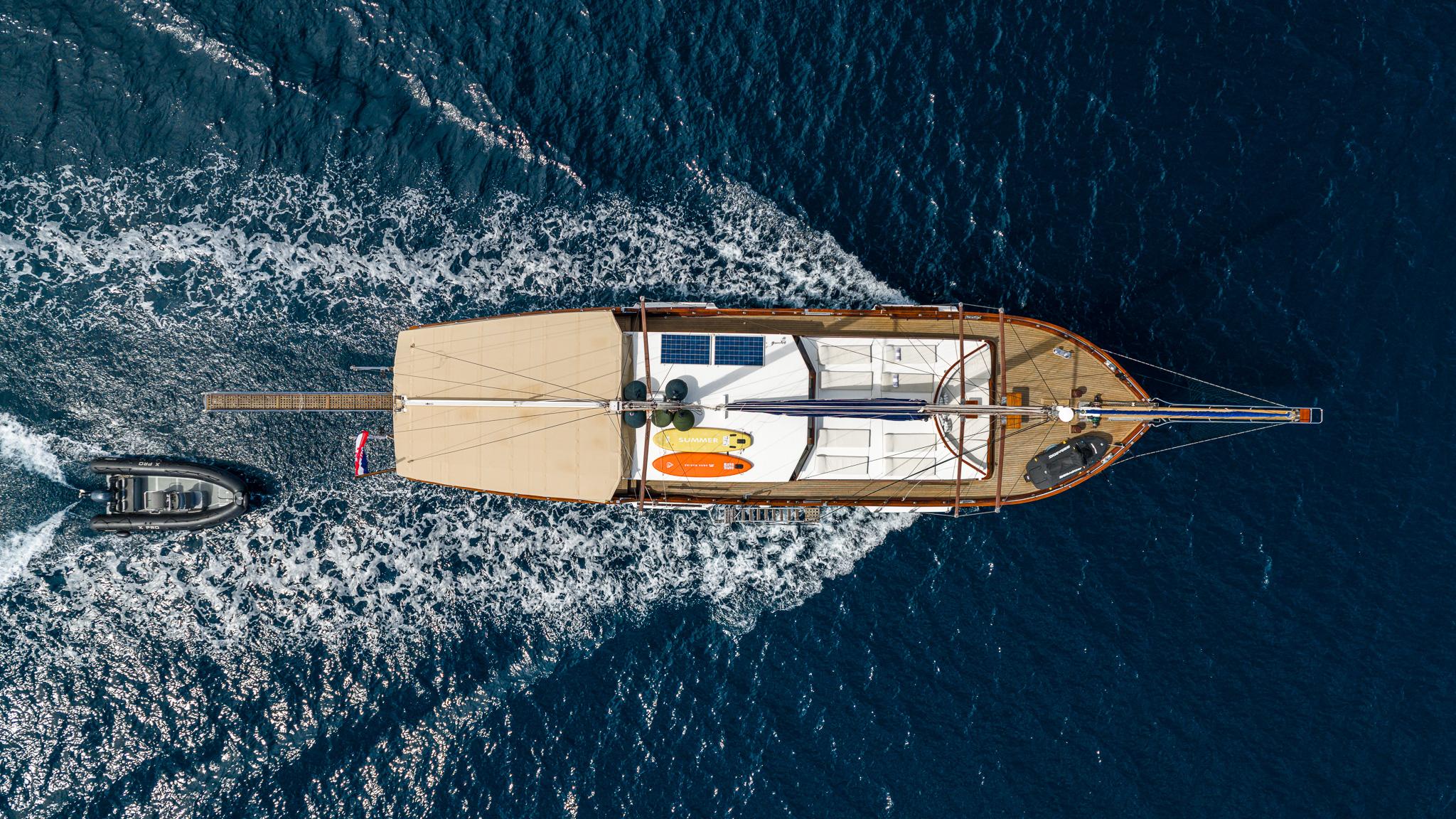 aerial view of traditional gulet yacht underway with tender alongside on blue water