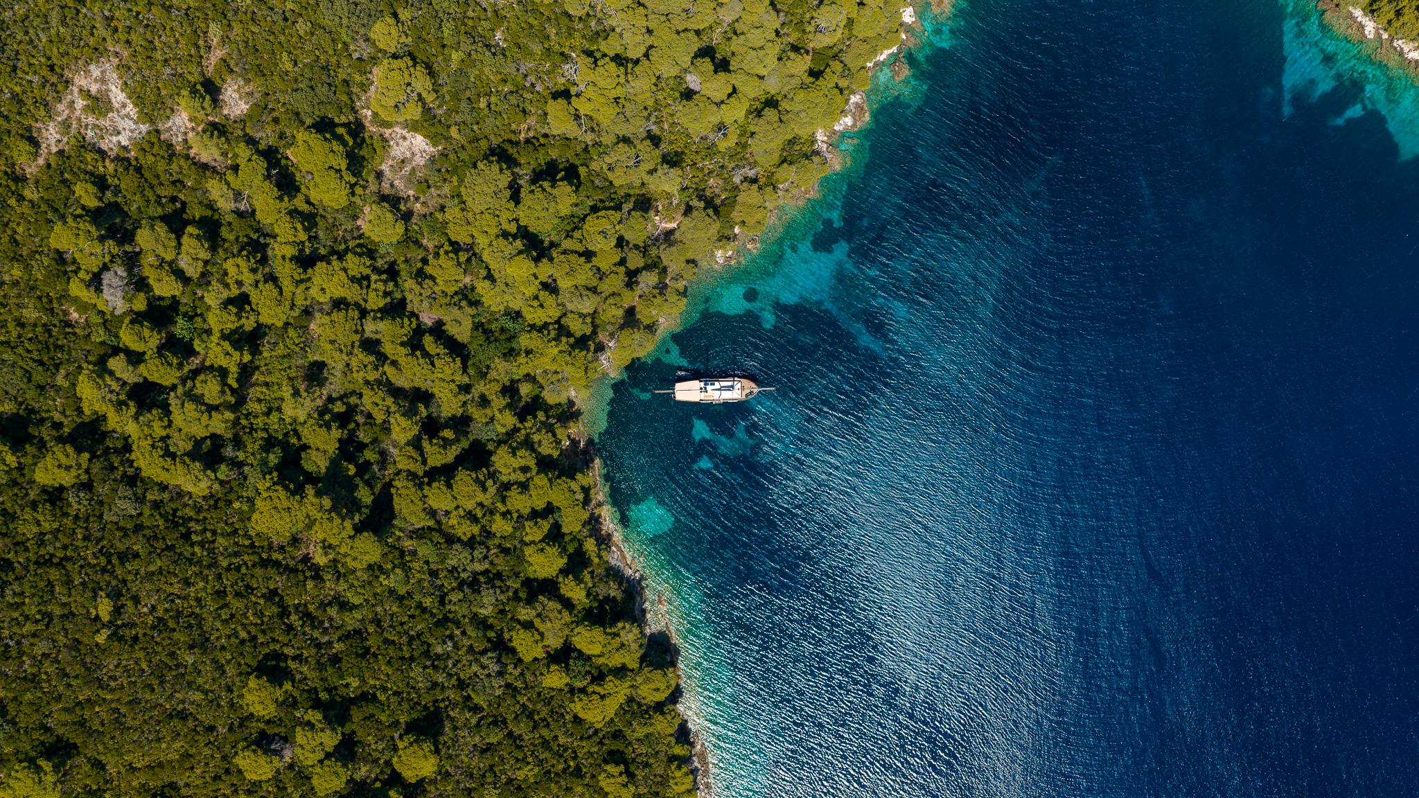 aerial view of white yacht anchored in crystal clear turquoise waters near forested coastline