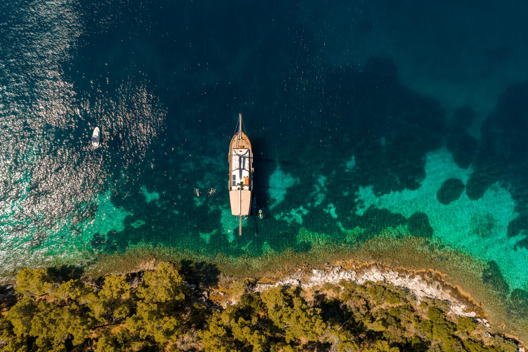 aerial view of traditional wooden gulet yacht anchored in crystal clear turquoise waters near Mediterranean coastline