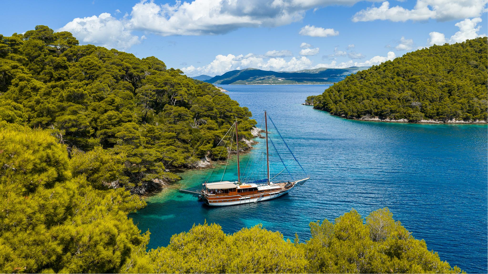 Aerial view of wooden gulet yacht anchored in turquoise bay surrounded by pine forests