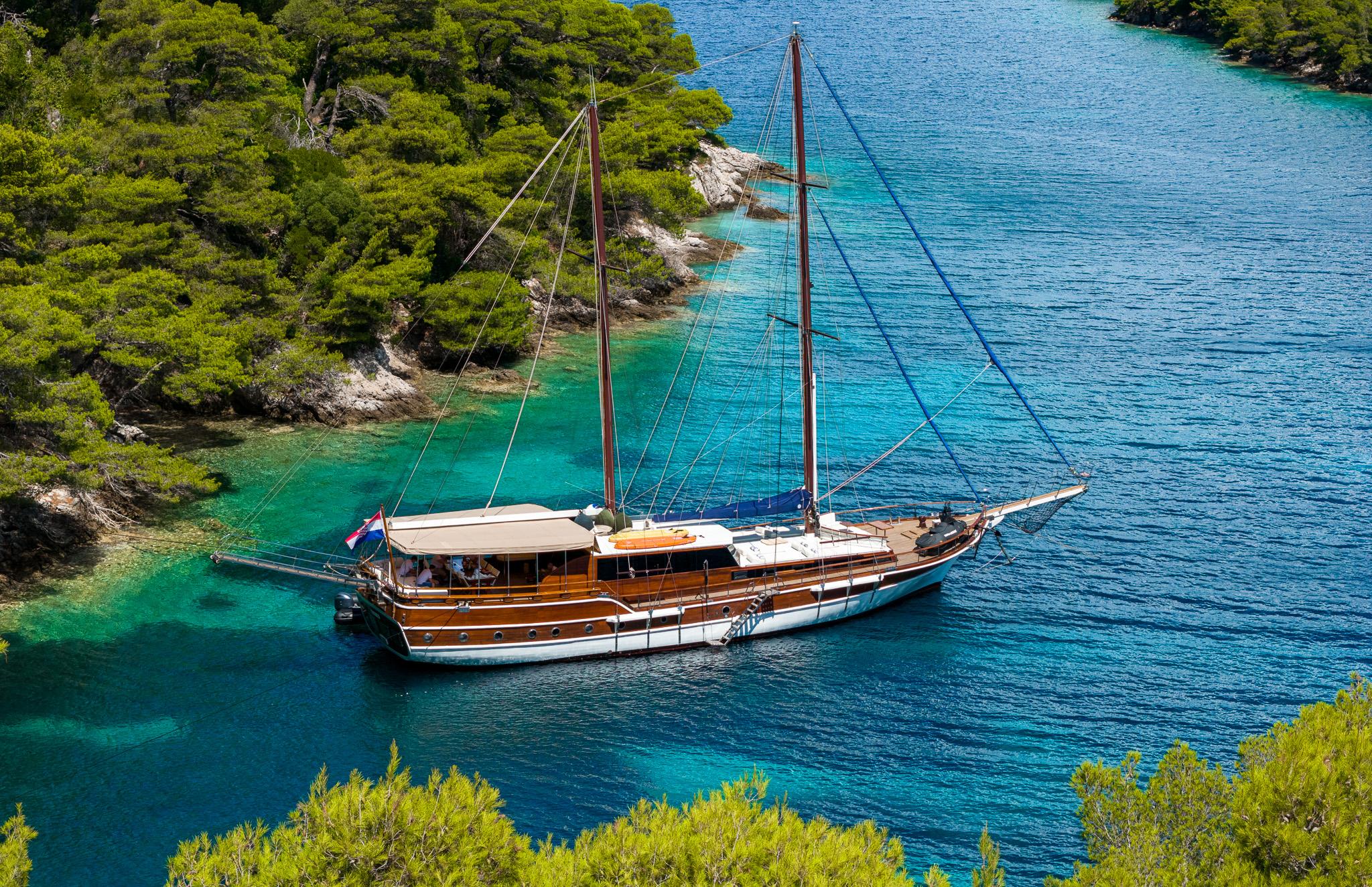 aerial view of wooden gulet with two masts anchored in crystal clear turquoise Mediterranean bay