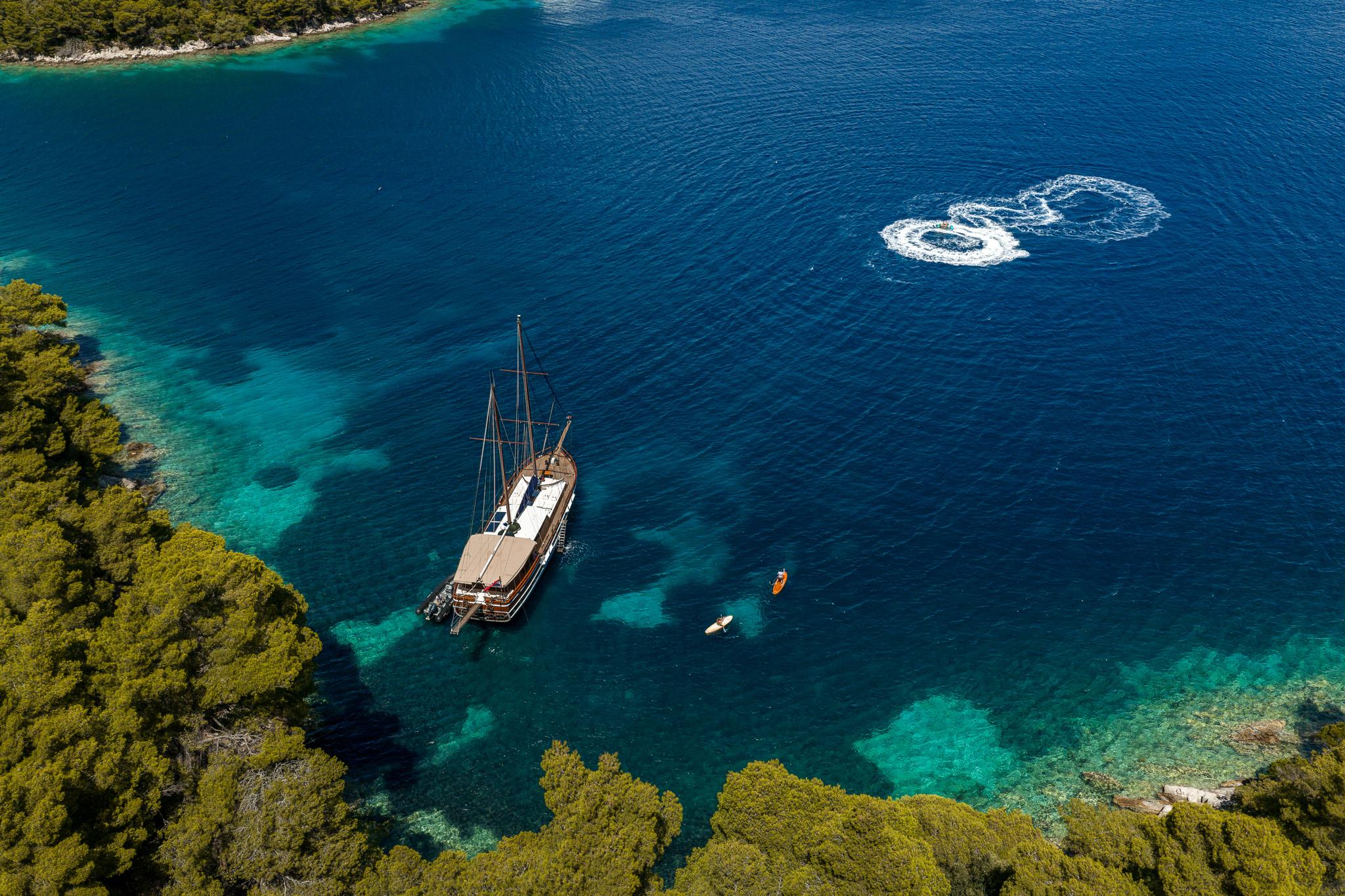 aerial view of traditional wooden gulet anchored in crystal clear turquoise bay with tender boats