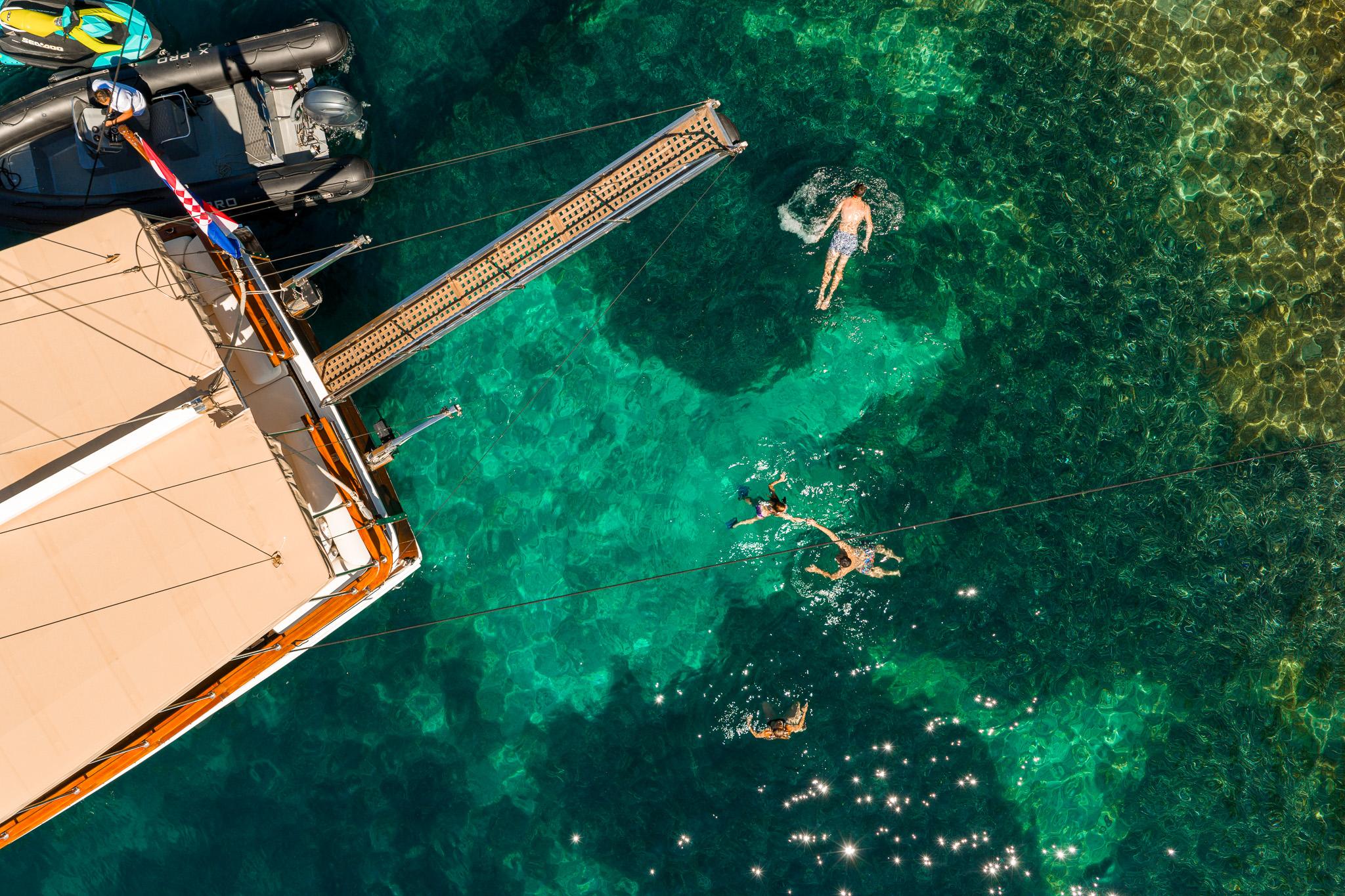 aerial drone shot of luxury yacht swimming platform with guests swimming in crystal clear turquoise waters