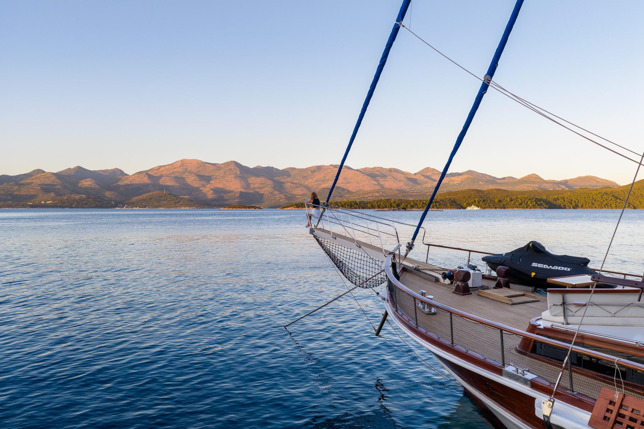 Traditional wooden gulet bow with blue mast rigging anchored in calm waters with mountainous coastline