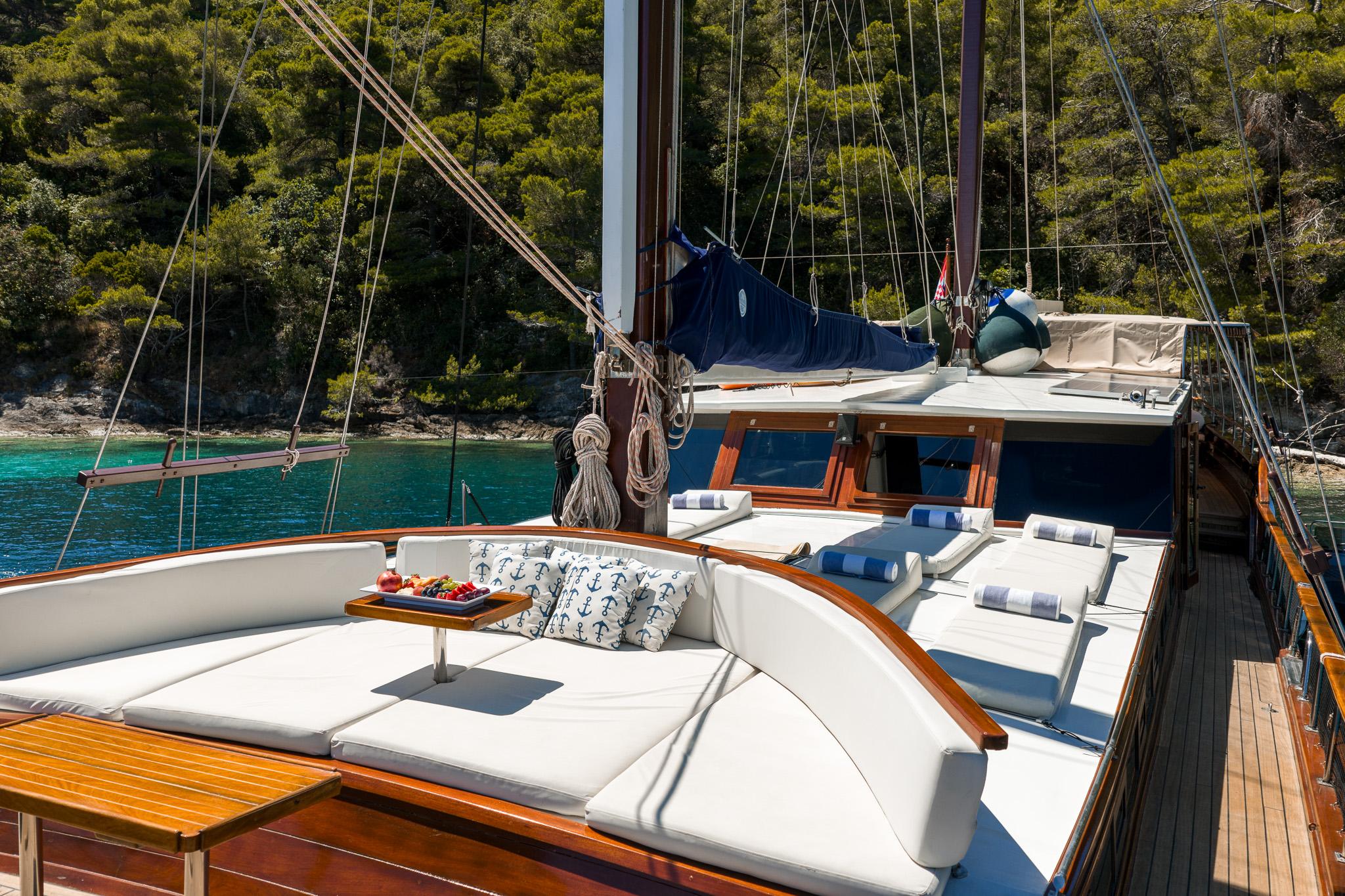 gulet aft deck with curved seating, white cushions, wooden table and nautical pillows
