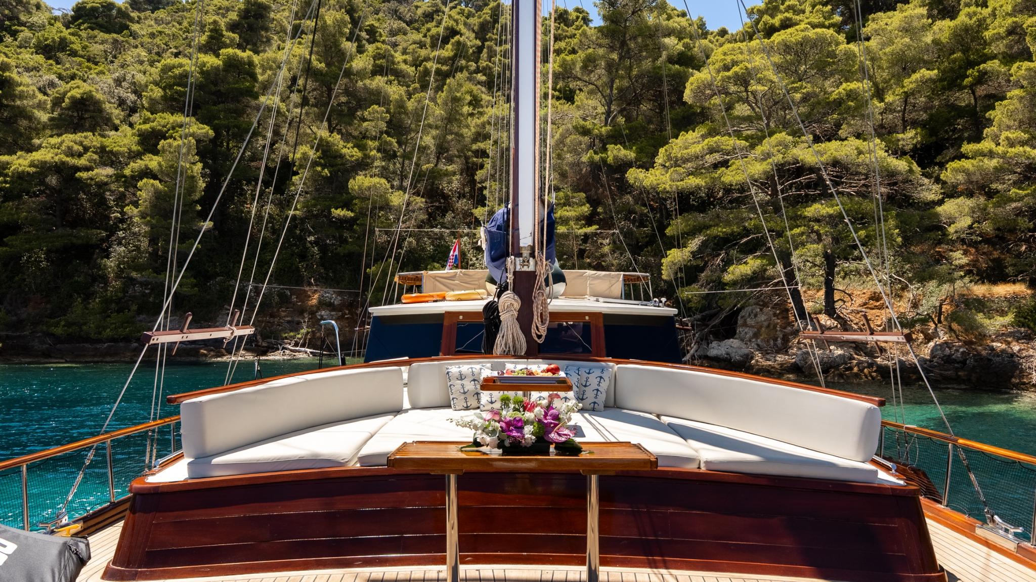 Traditional gulet bow deck with curved white cushioned seating and wooden table in turquoise bay