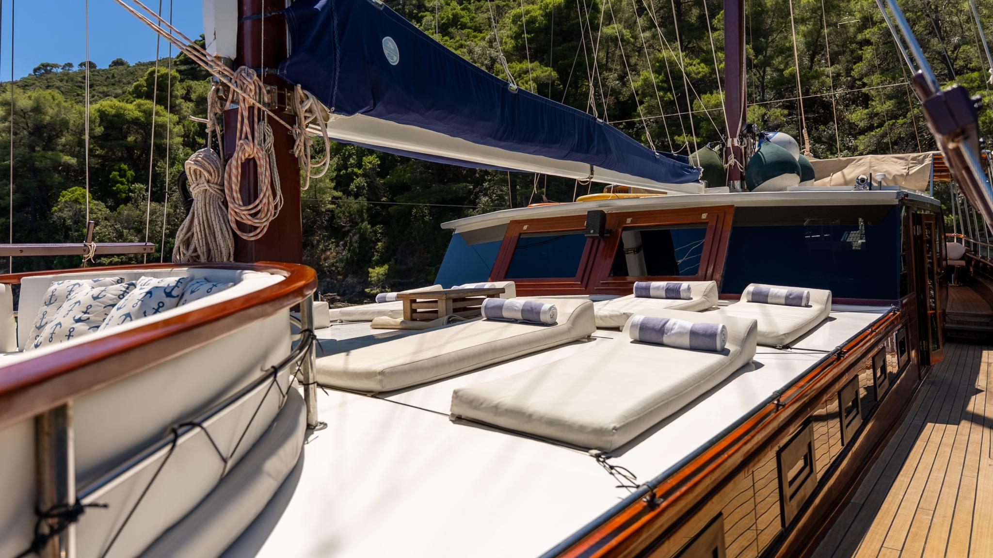 Gulet foredeck with white sun loungers, blue striped cushions and towels, wooden deck