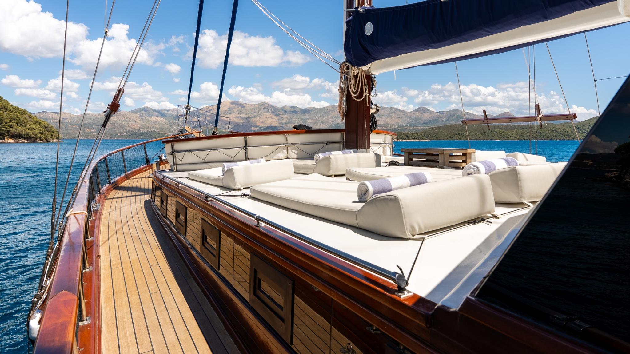 gulet sun deck featuring white sunbeds with rolled towels and traditional sailing rigging