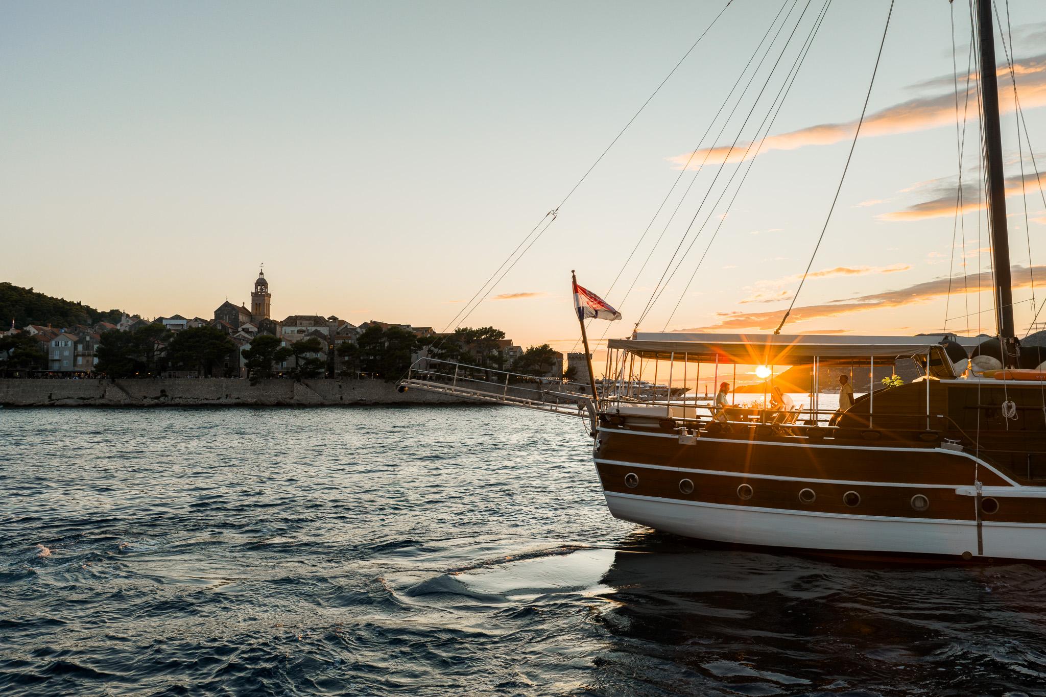 Traditional wooden gulet moored in harbor at sunset with historic coastal town backdrop