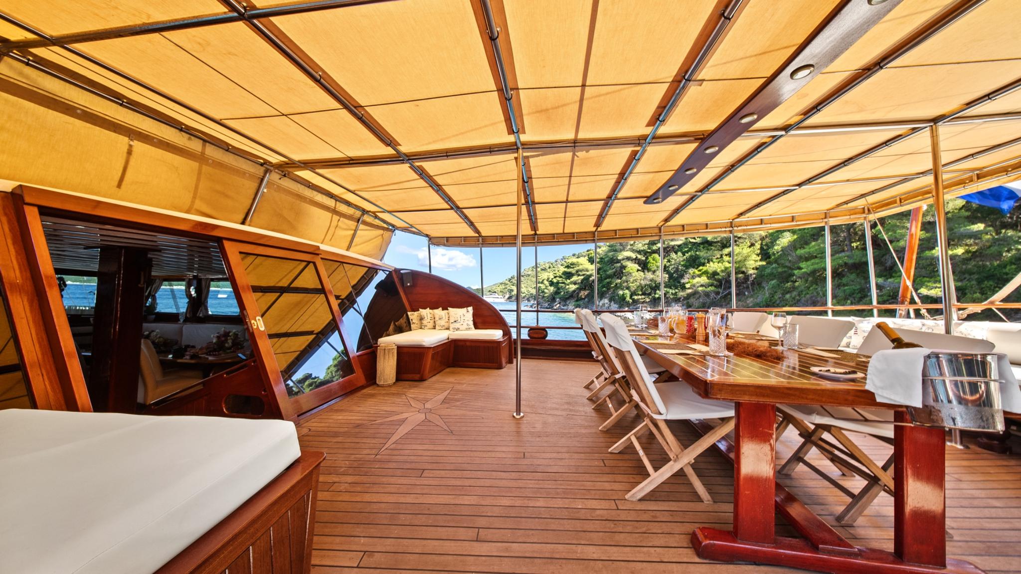luxury gulet aft deck with wooden dining table, folding chairs under cream awning