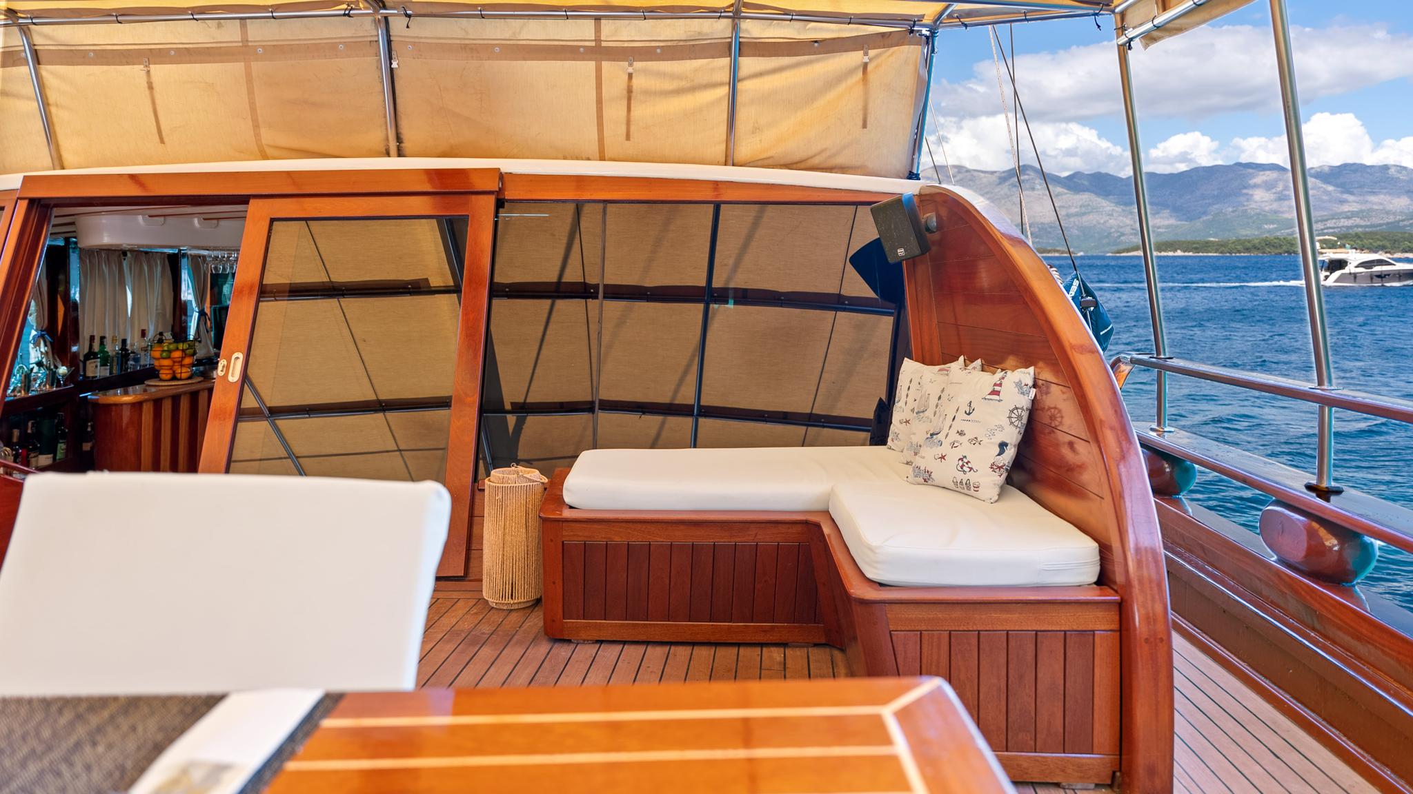 gulet aft deck with curved wooden banquette seating, white cushions and nautical pillows