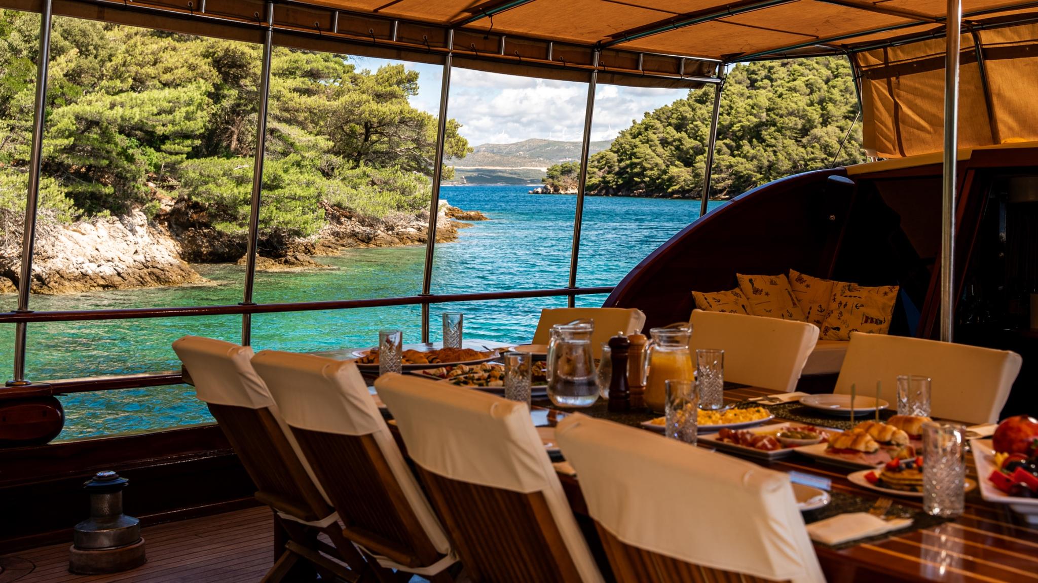 Gulet dining table set with breakfast spread overlooking turquoise Mediterranean bay