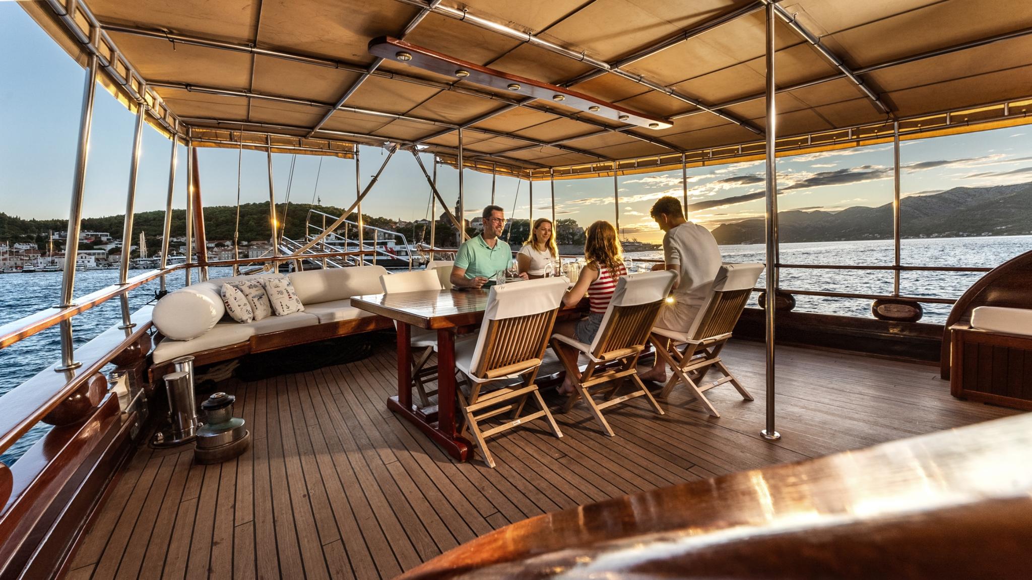 Gulet aft deck with dining table, teak chairs, and guests enjoying evening conversation under awning