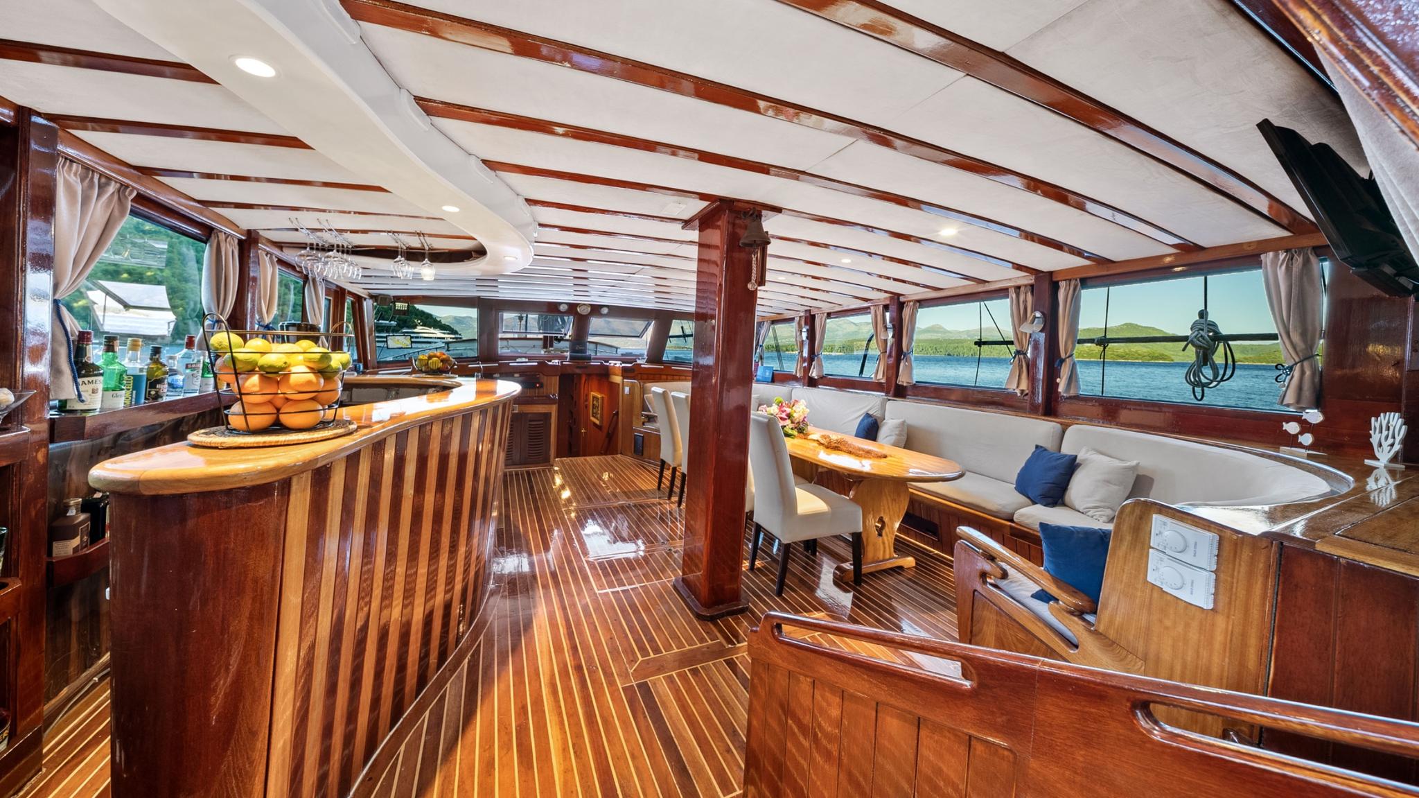 luxury yacht main salon with curved dining seating, galley bar, and exposed beam ceiling