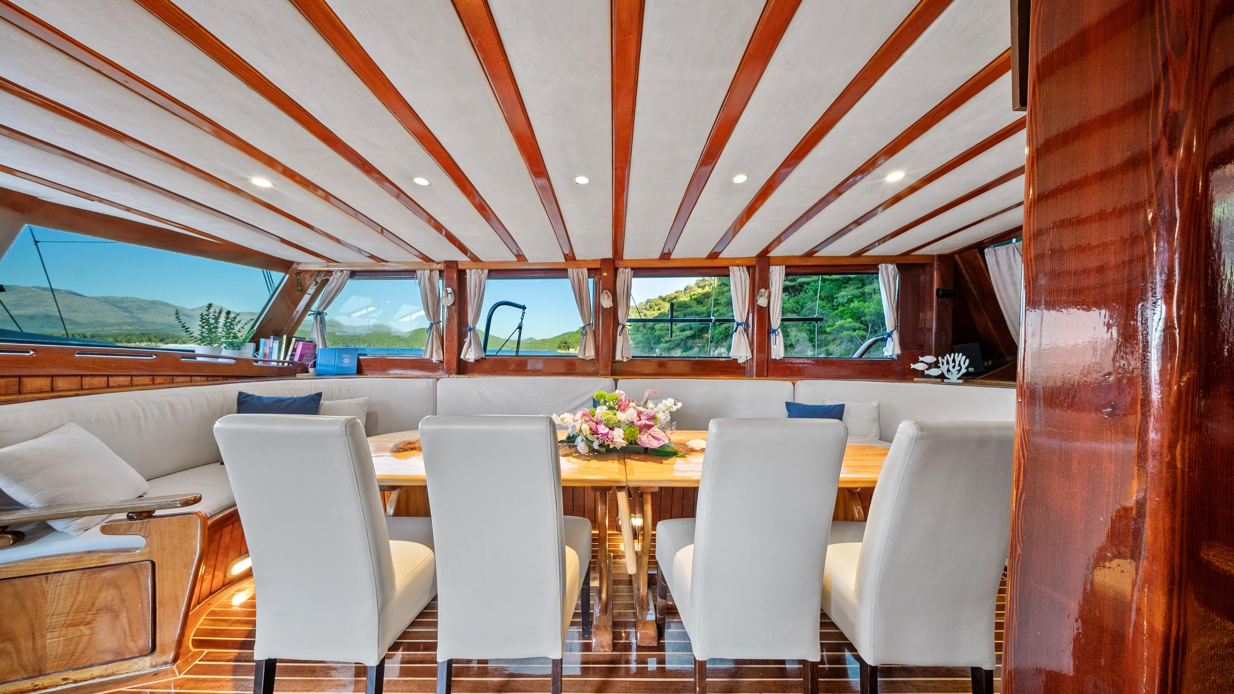 yacht salon interior with wooden dining table, white chairs and bench seating
