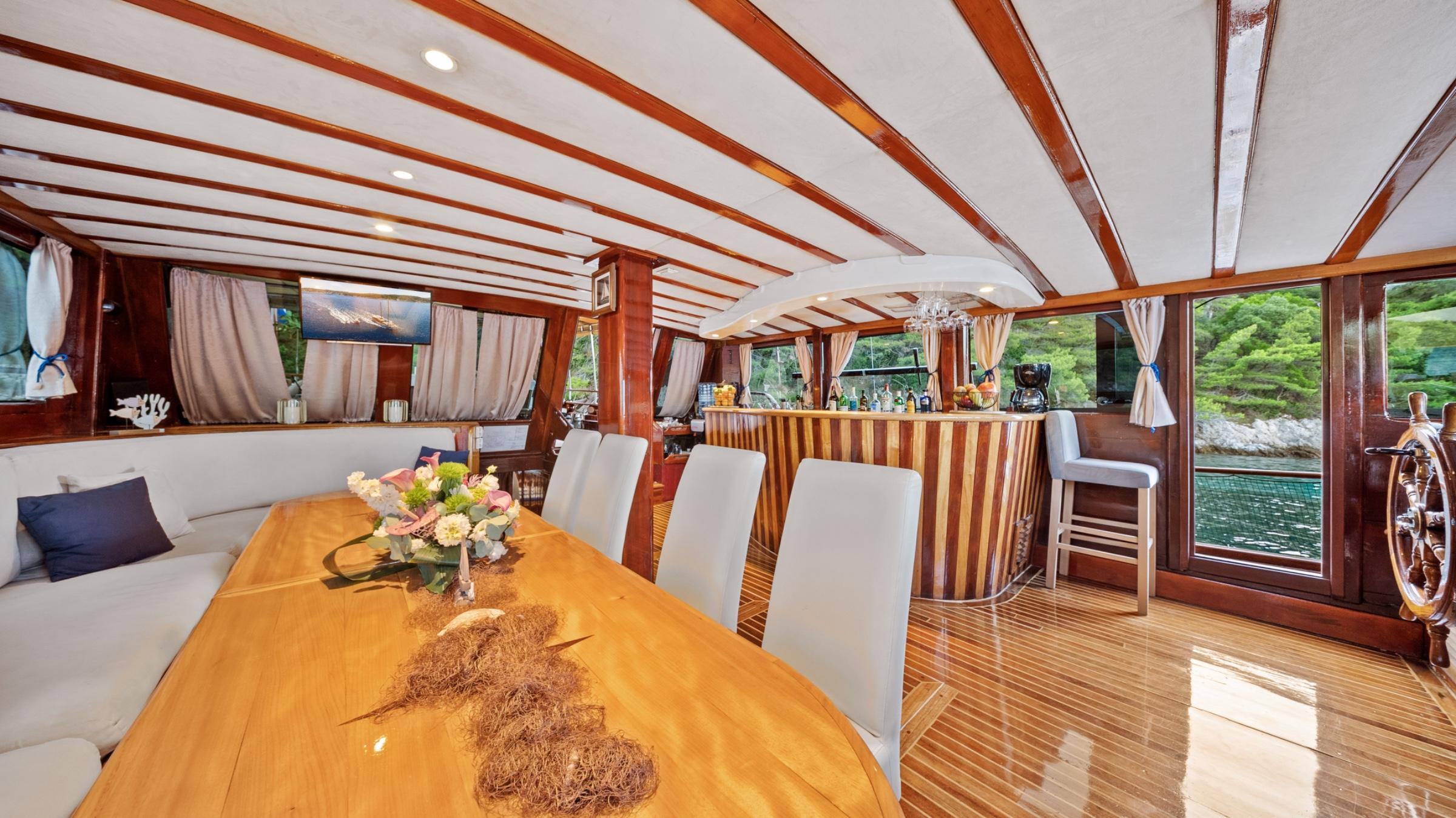 gulet main salon with wooden dining table, white chairs, built-in bar, and panoramic windows