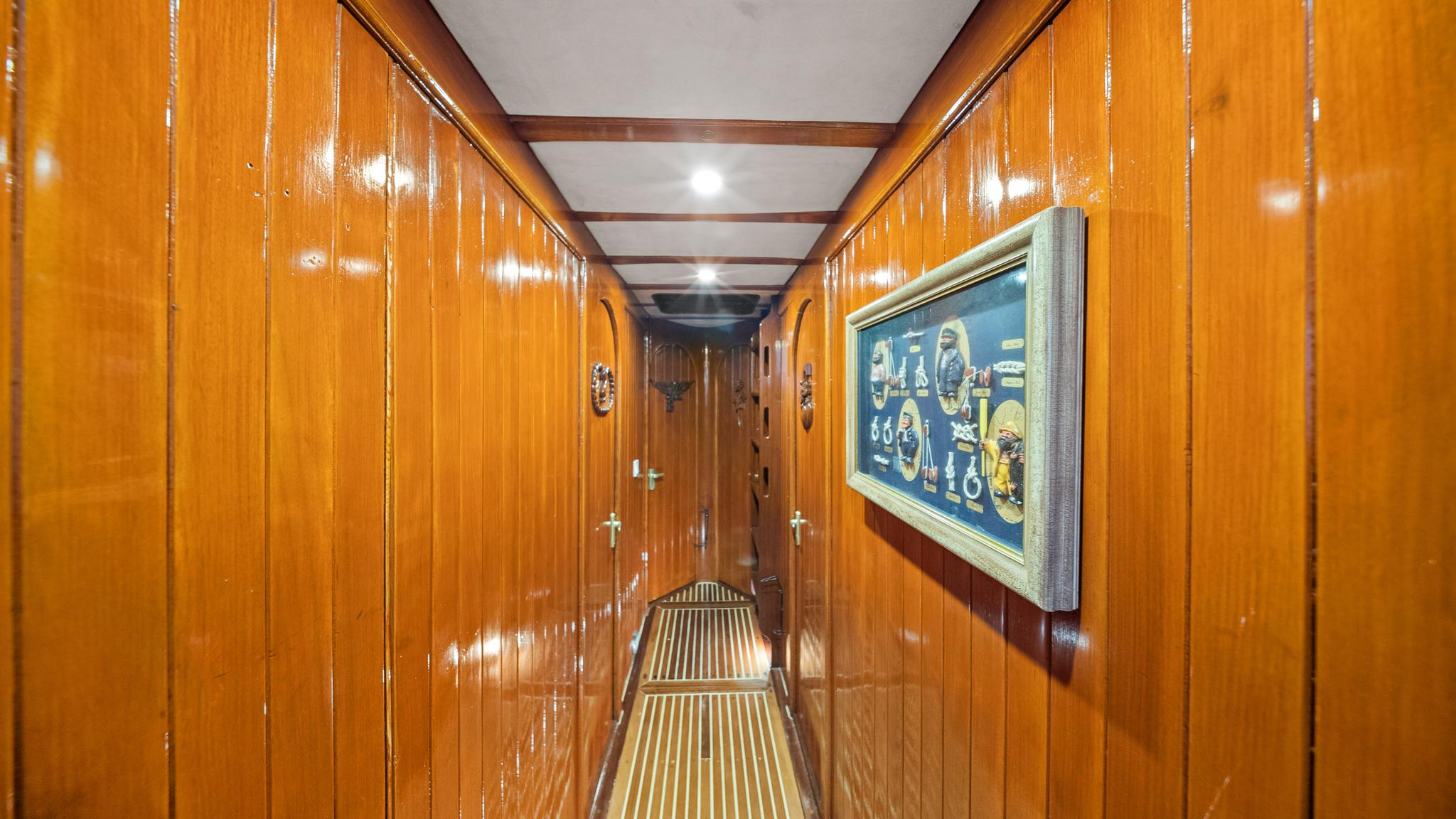 yacht interior corridor with polished wood paneling, cabin doors, and nautical artwork on walls
