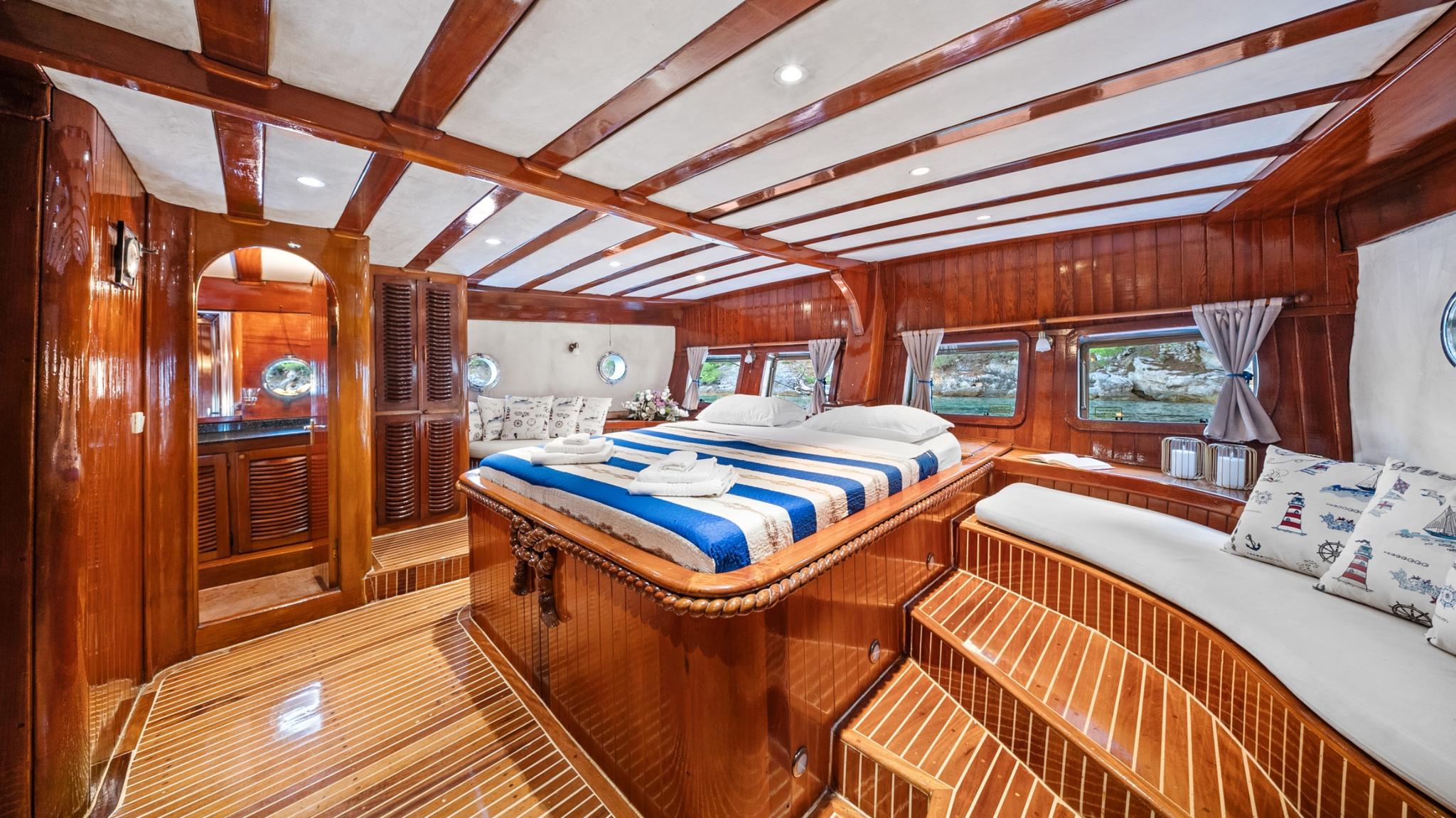 luxury yacht cabin with double bed, curved bench seating, wooden paneling and portholes