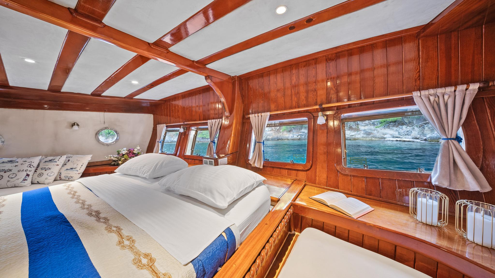 yacht cabin with double bed, white linens, panoramic windows showing coastline views