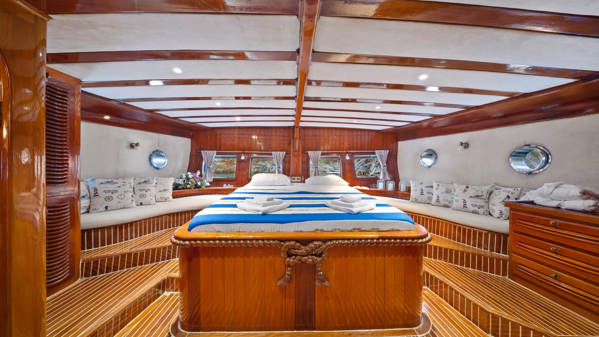 master cabin interior with king bed, white and blue bedding, wooden paneling and circular portholes