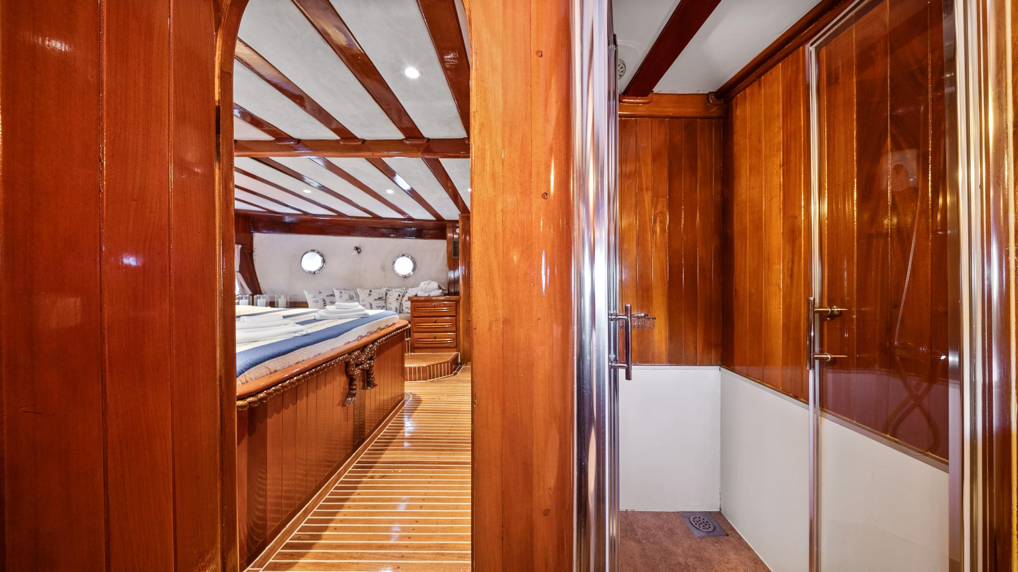 yacht interior corridor with rich wood paneling leading to cabin with bed and portholes