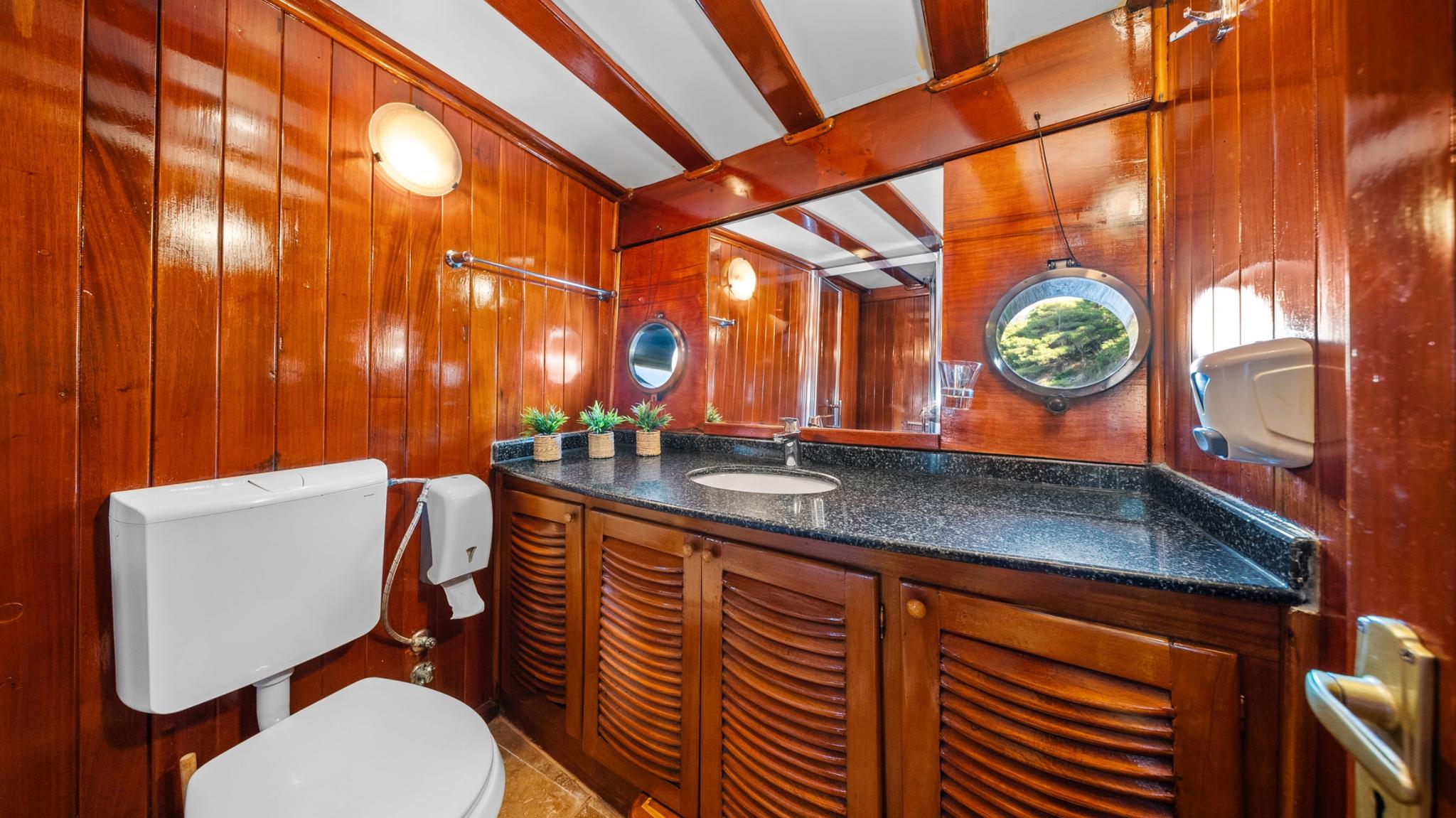 yacht bathroom featuring dark granite countertop, wooden cabinetry, round porthole window, and white toilet