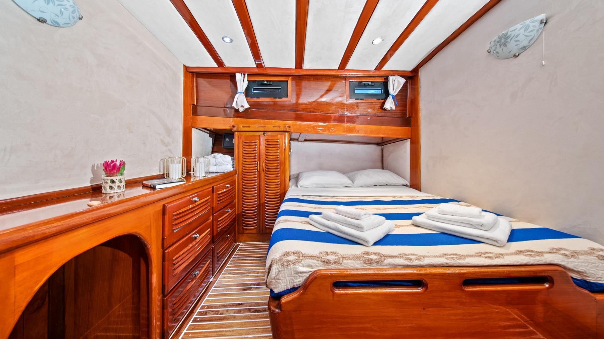 yacht guest cabin featuring double bed with blue striped bedding and teak cabinetry