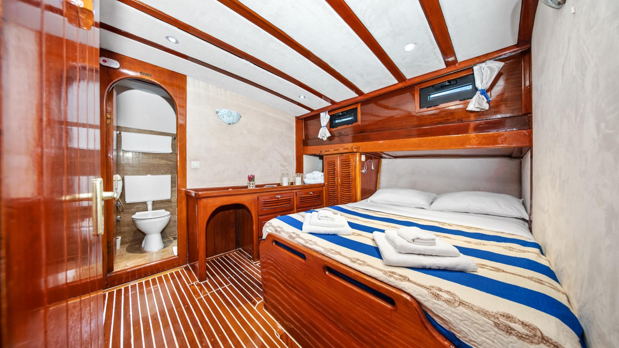 yacht guest cabin featuring double bed with blue striped bedding and adjoining en-suite bathroom