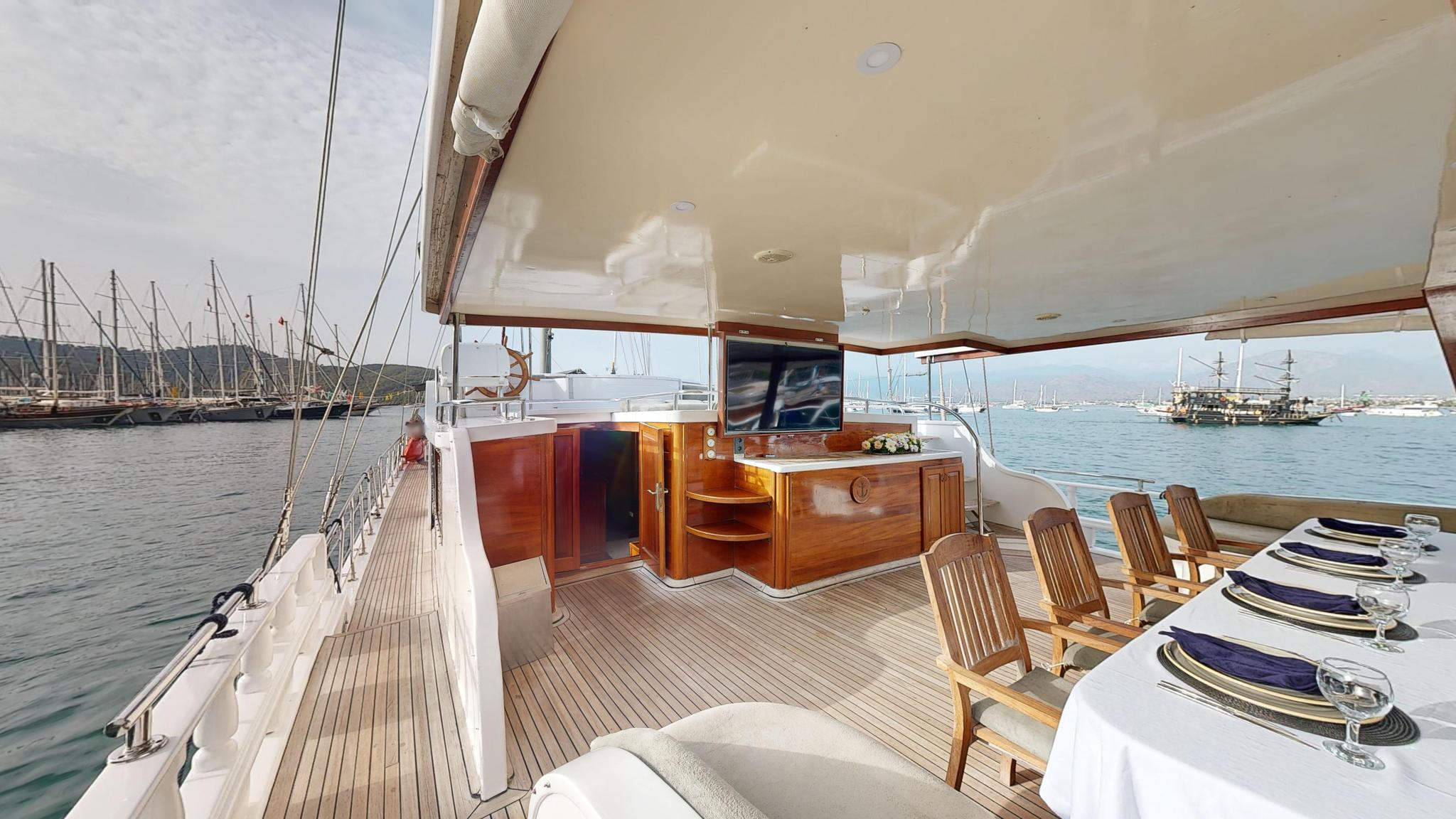 Gulet covered aft deck with formal dining table, wooden bar counter, and marina views
