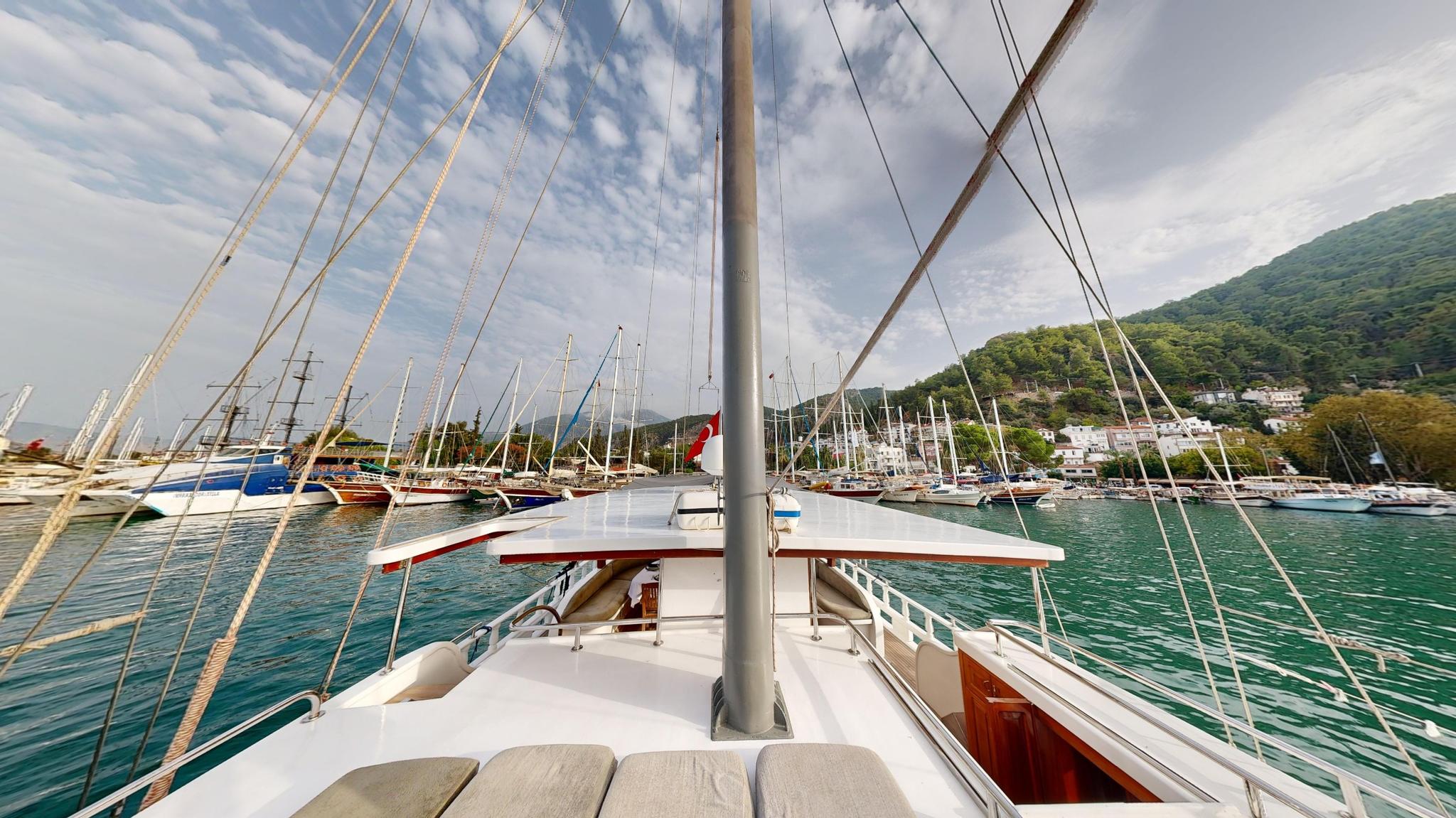 gulet forward deck with central mast, rigging lines, and harbor view with mountains