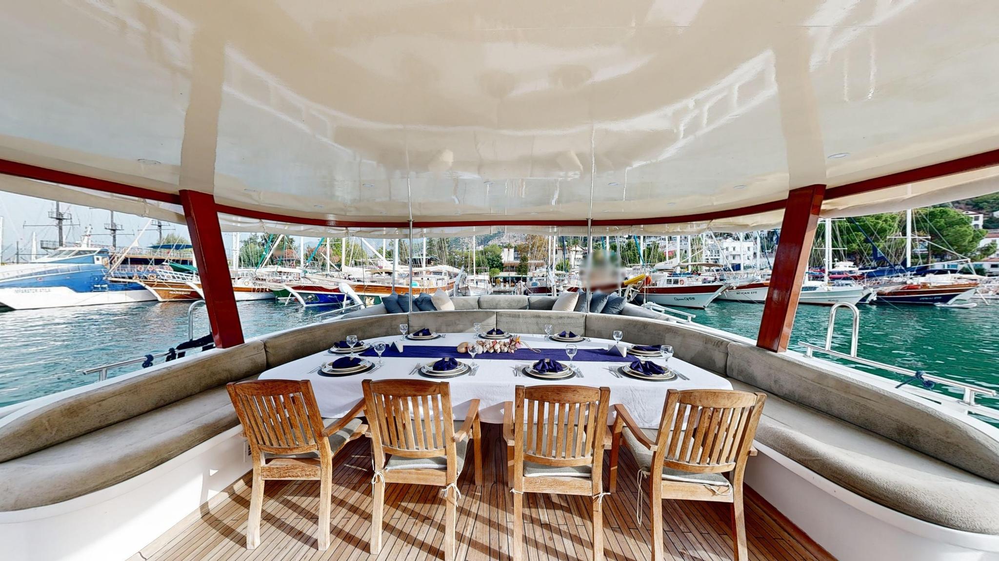covered aft deck dining table with formal place settings and curved seating overlooking marina