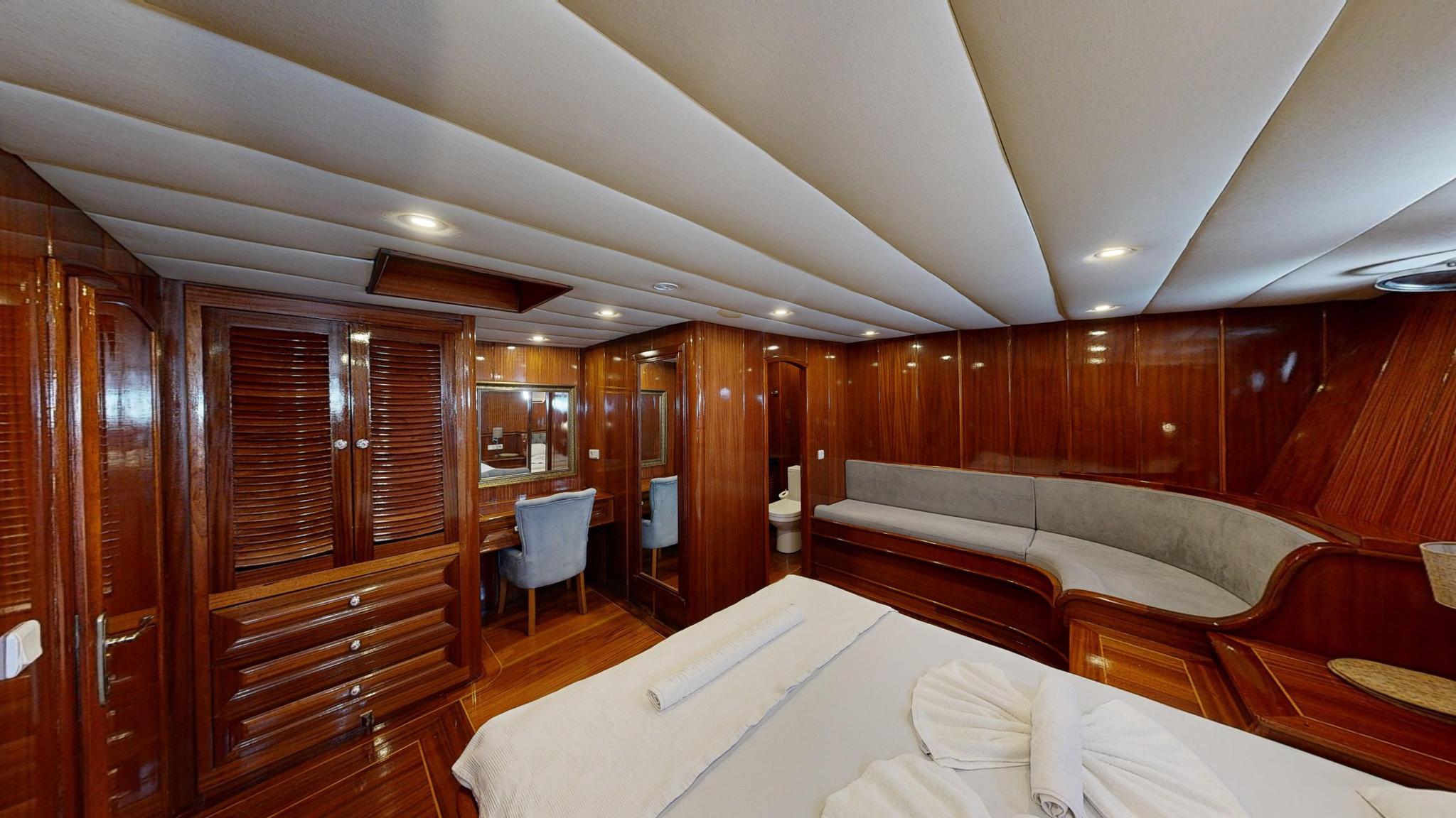 yacht cabin interior with double bed, built-in seating, vanity desk and mahogany paneling