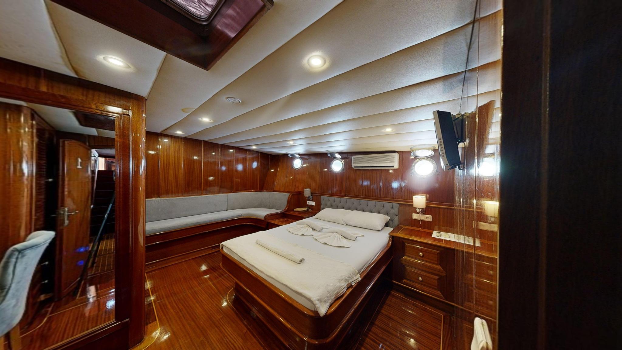 Master cabin interior with double bed, curved seating area, rich wood paneling and recessed lighting