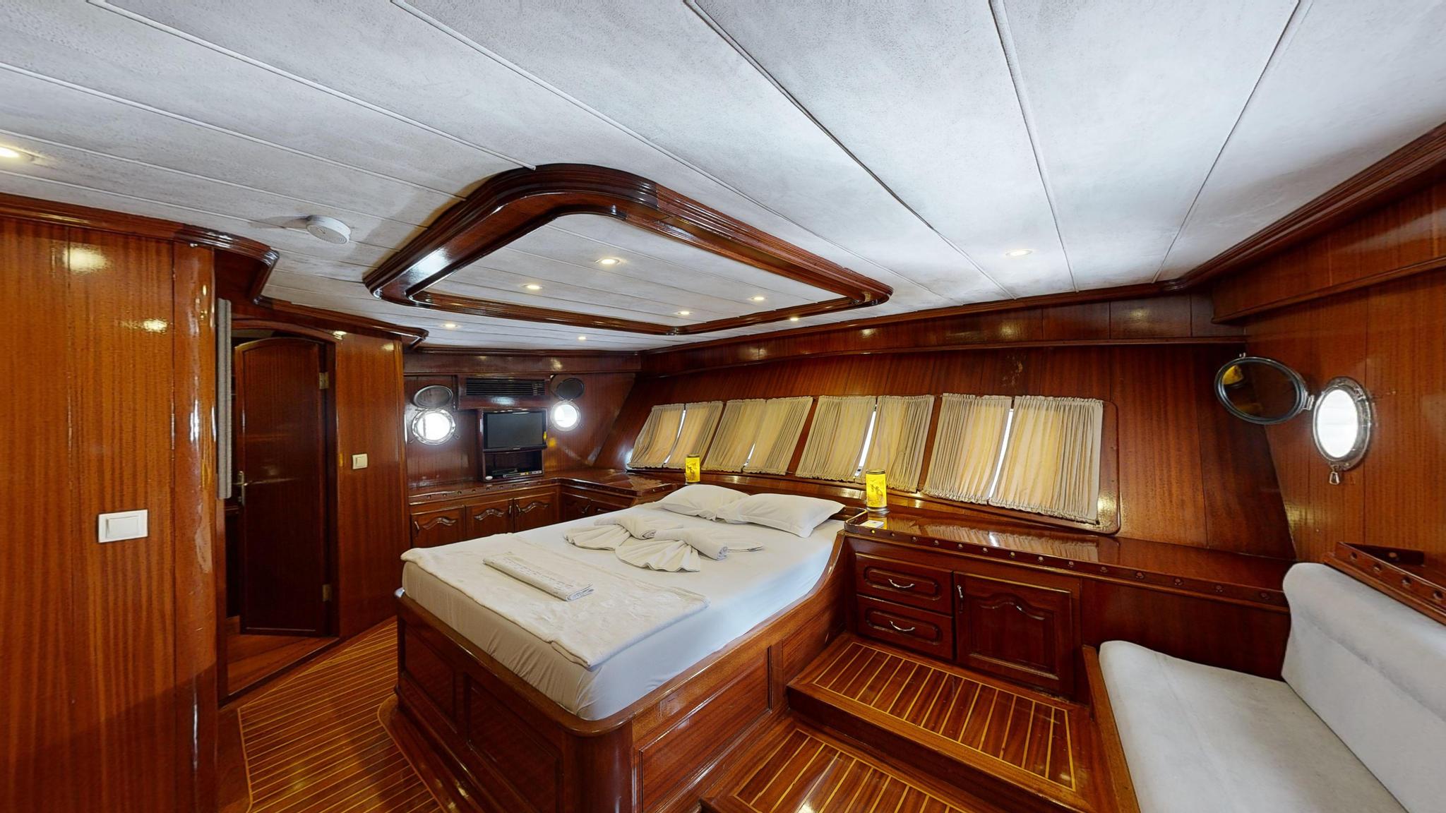 luxury yacht master cabin featuring king bed, rich wood paneling, built-in storage and portholes