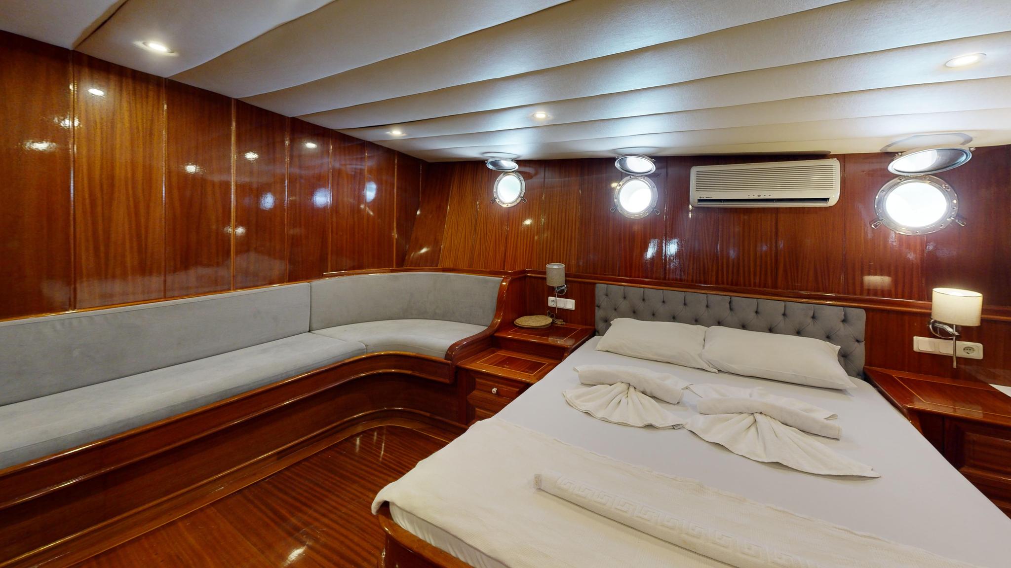 yacht cabin interior with double bed, grey upholstered seating, portholes and wood paneling