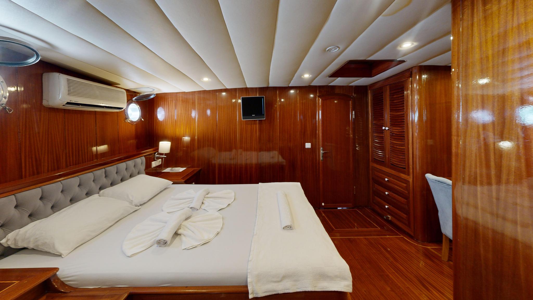 yacht guest cabin with double bed, gray tufted headboard, and polished wood walls