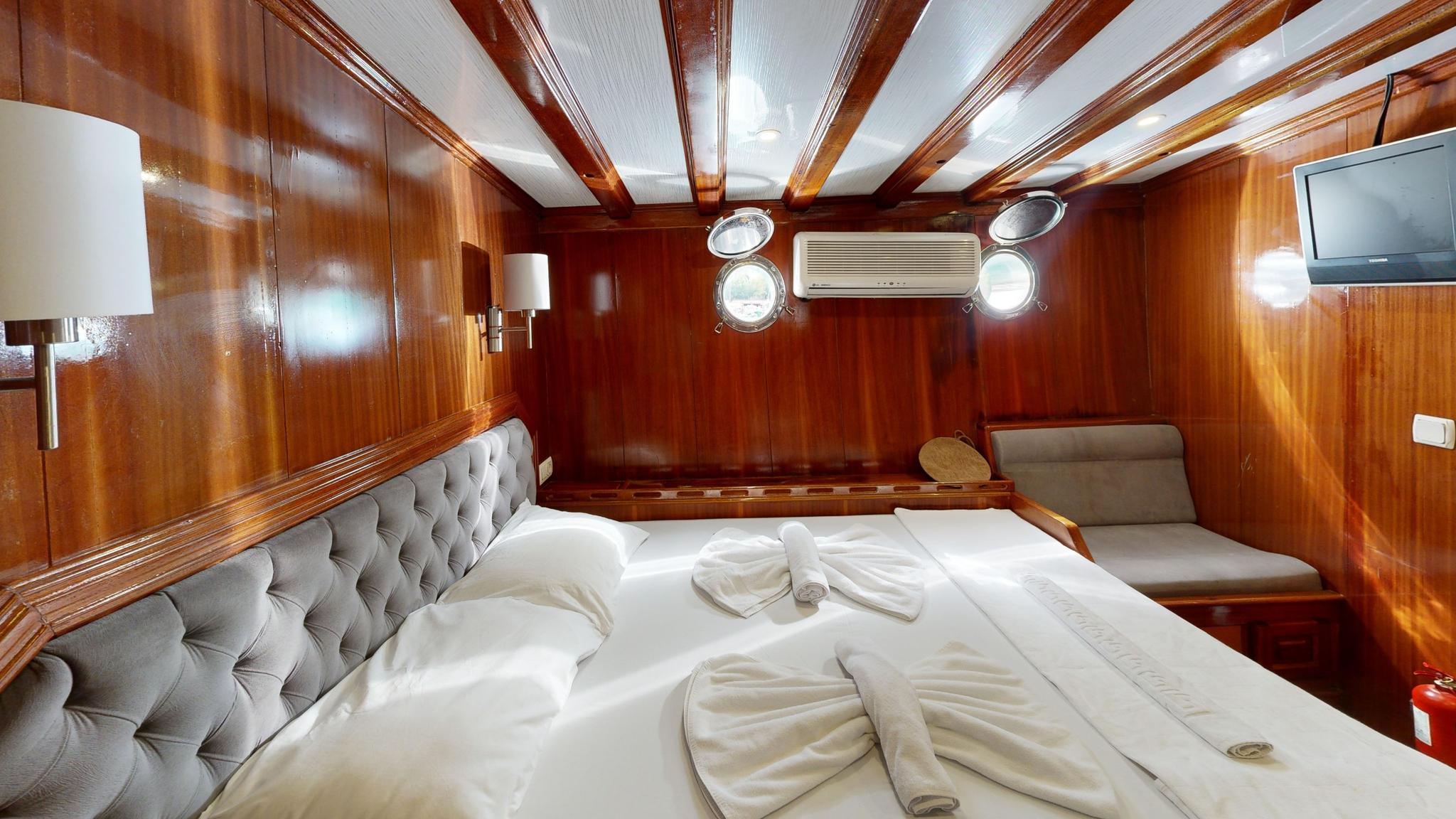 yacht cabin interior with double bed, tufted grey headboard, wood paneling and portholes