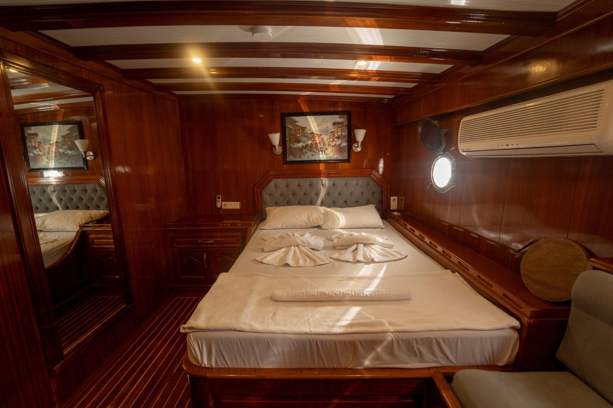 yacht cabin interior with double bed, tufted grey headboard, rich wood paneling and porthole