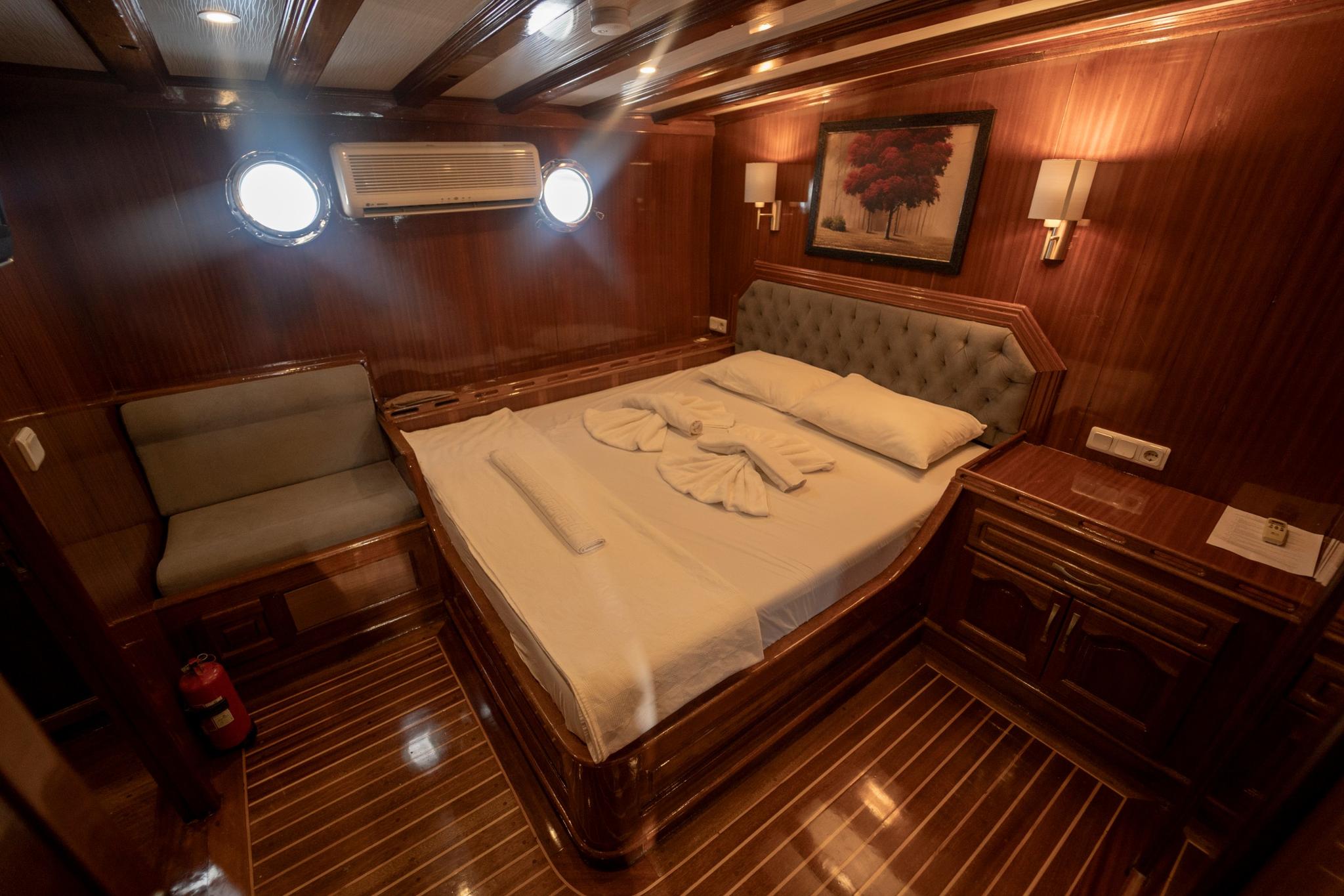 yacht guest cabin interior with double bed, tufted headboard, built-in seating and portholes
