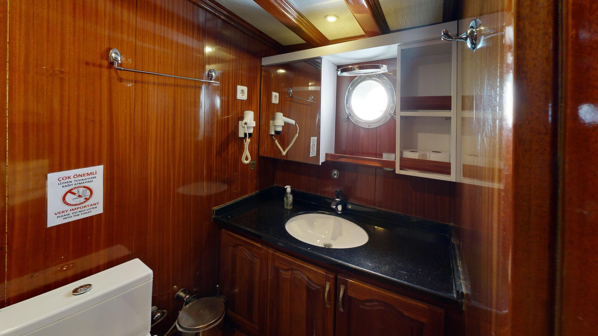 yacht bathroom with black granite vanity, round basin, porthole window and wooden paneling
