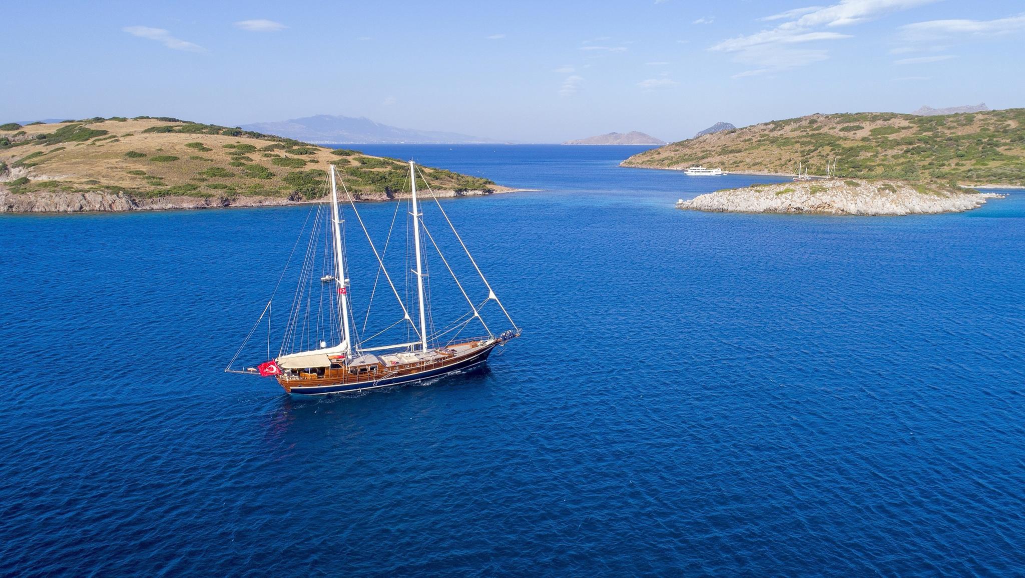 aerial view of wooden gulet yacht anchored in turquoise Mediterranean waters near rugged coastline
