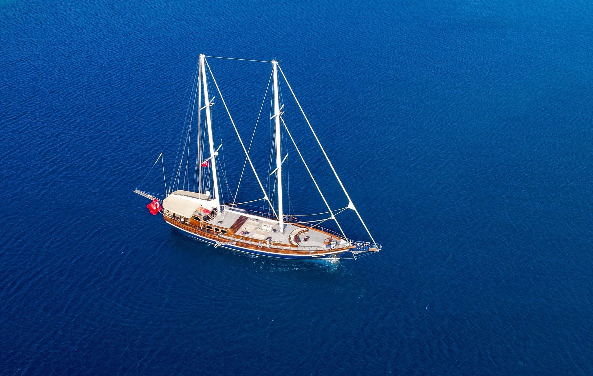 aerial view of traditional wooden gulet with two masts anchored in deep blue waters