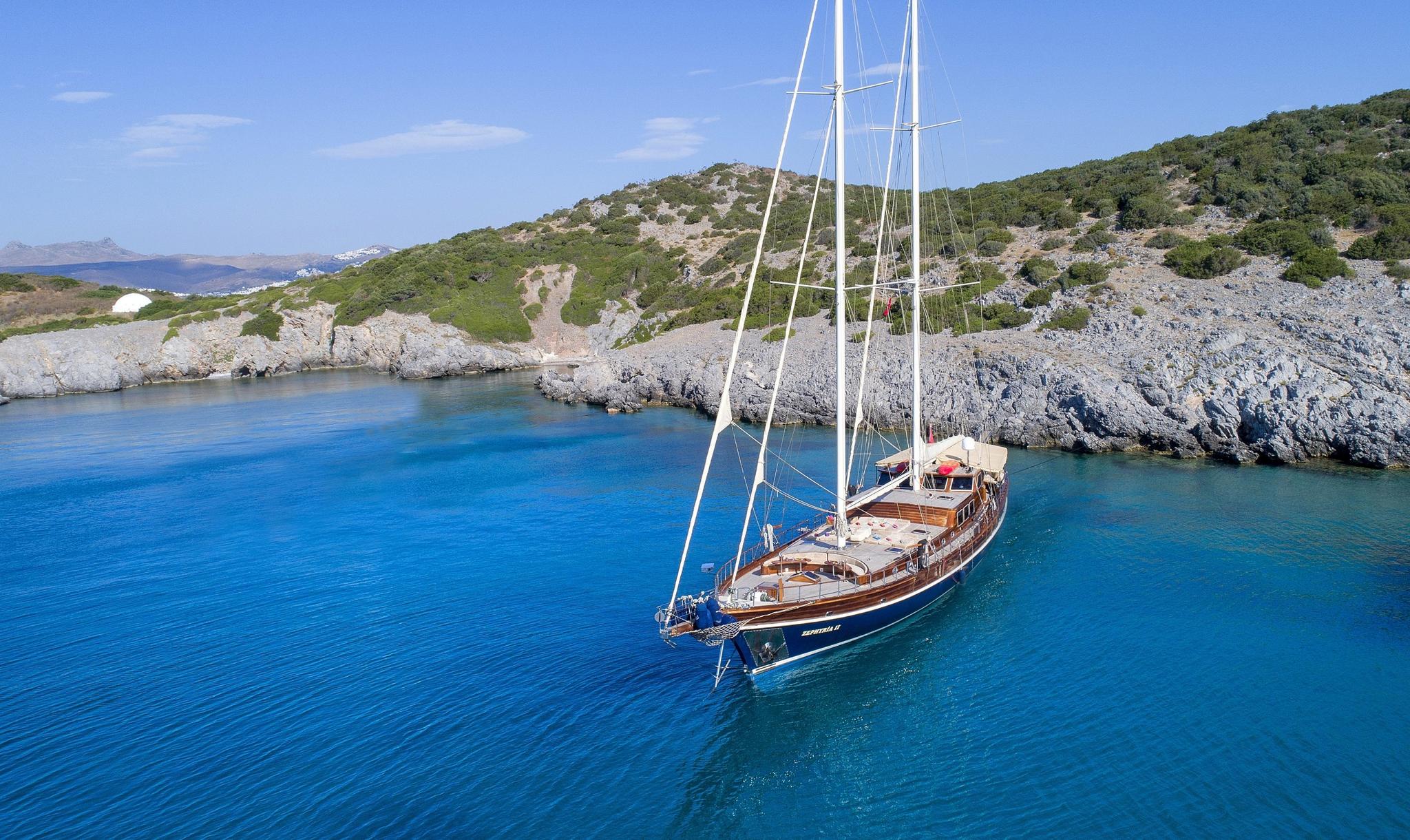 aerial view of traditional wooden gulet yacht anchored in crystal clear turquoise bay with rocky coastline