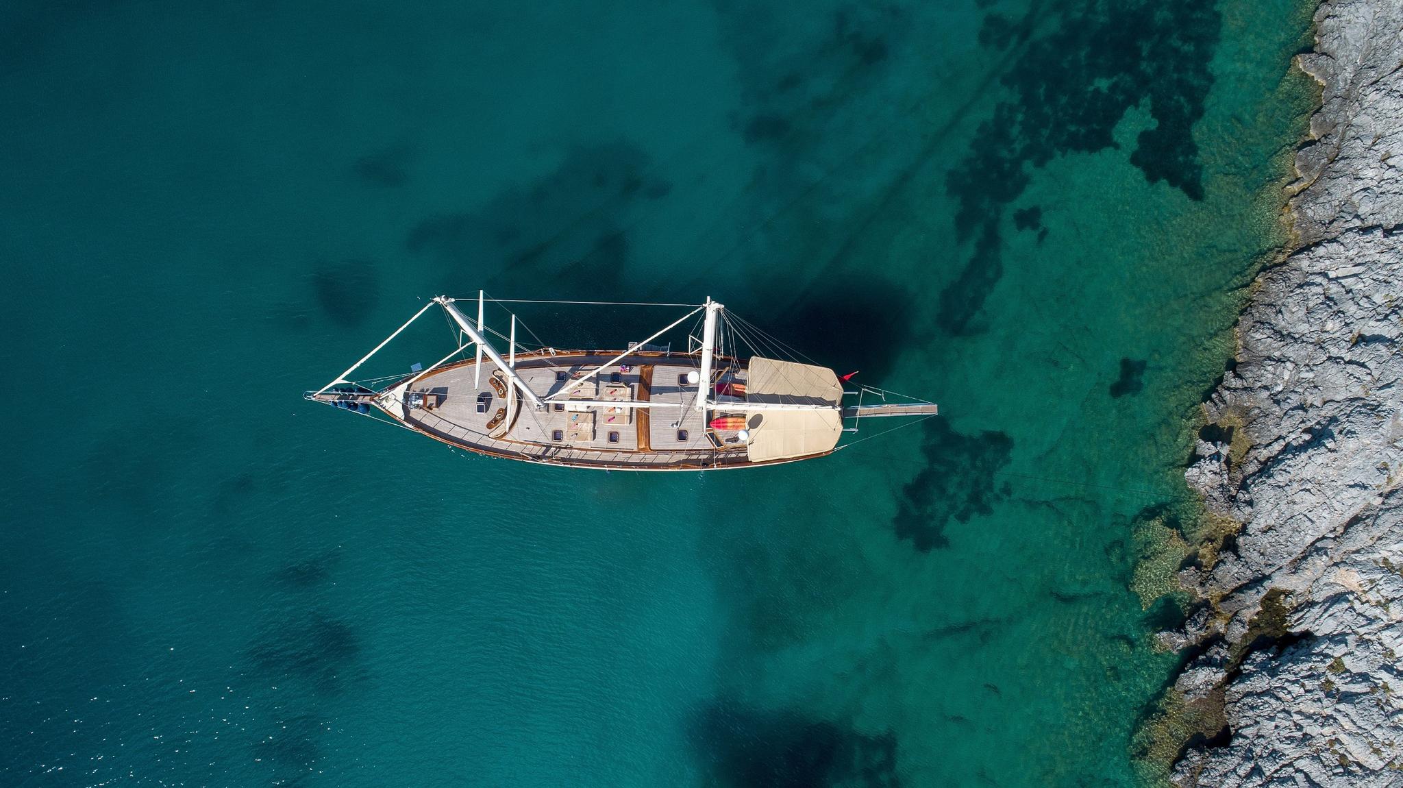 aerial view of traditional wooden gulet yacht anchored in crystal clear turquoise waters near rocky coastline