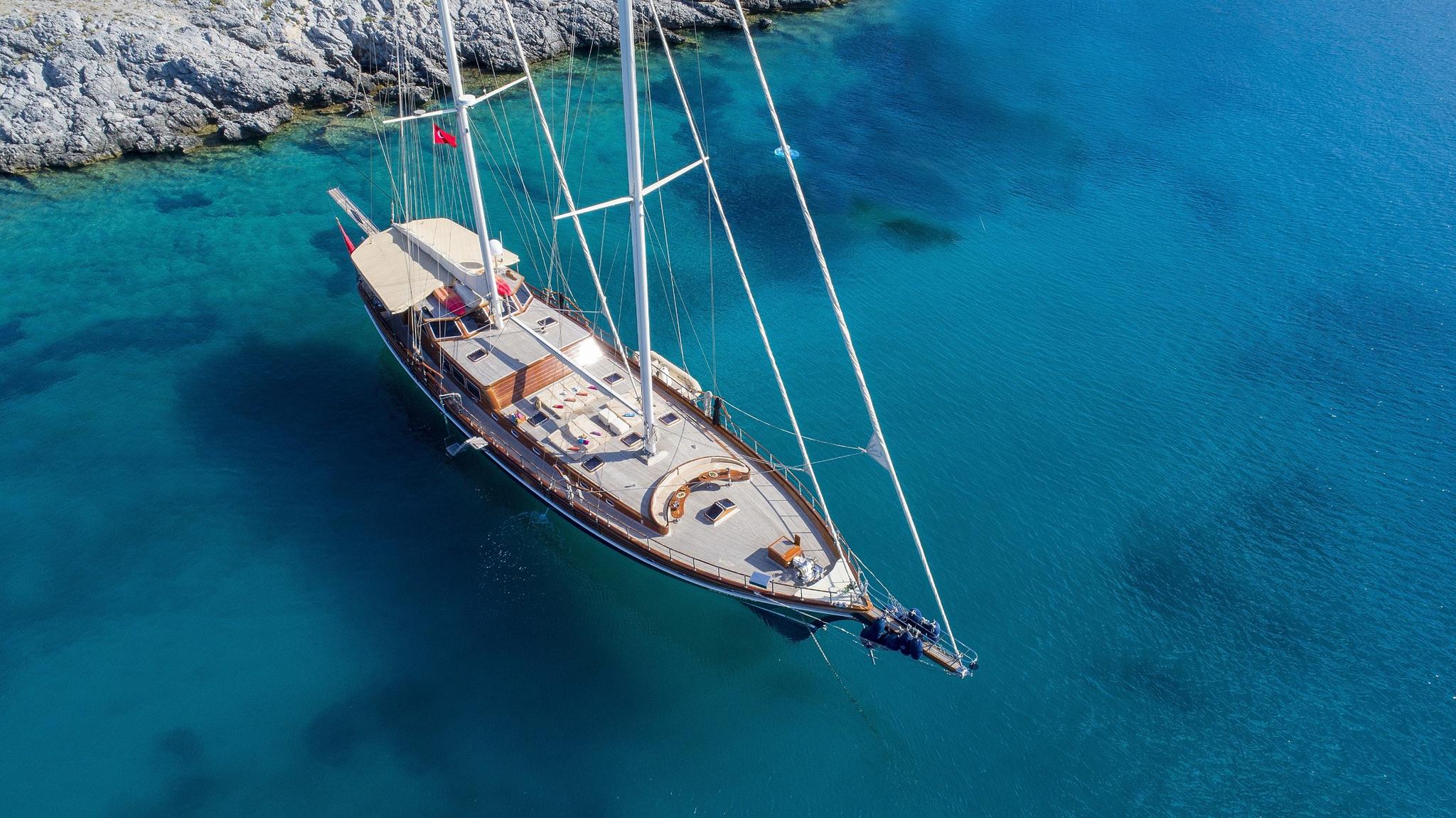 Aerial view of traditional wooden gulet yacht anchored in crystal clear turquoise Mediterranean waters near rocky coastline