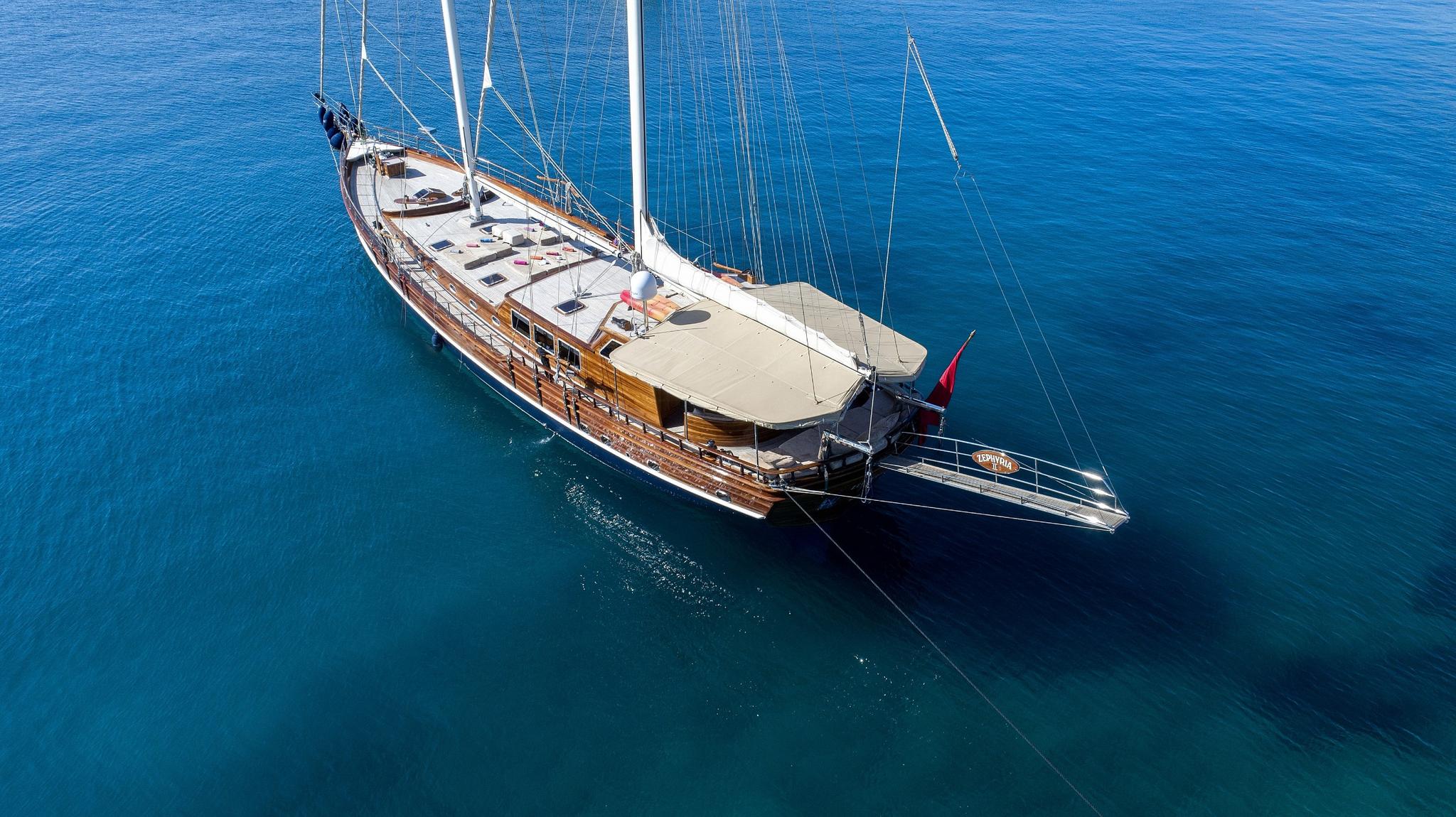 aerial view of traditional wooden gulet with white sails anchored in crystal clear blue waters