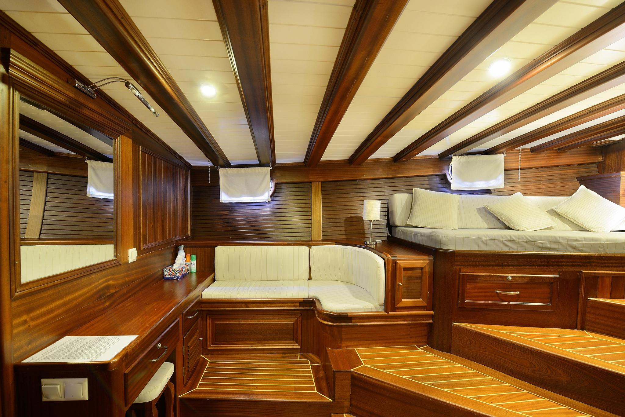 yacht cabin interior with built-in bed, upholstered seating and dark wood paneling