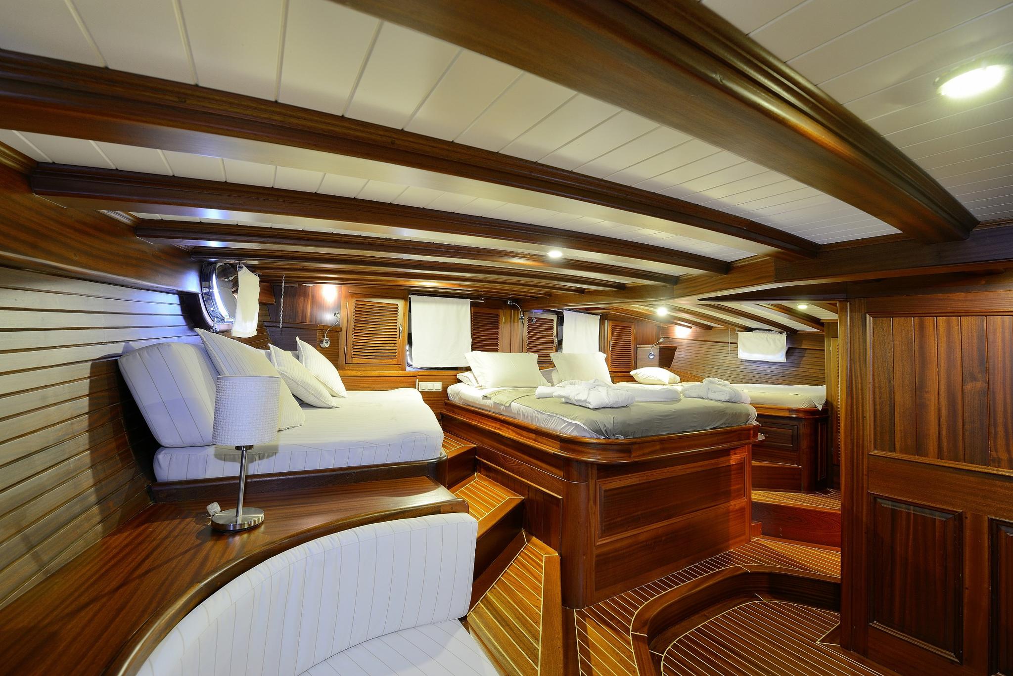 yacht guest cabin featuring twin beds with white bedding and rich teak wood paneling
