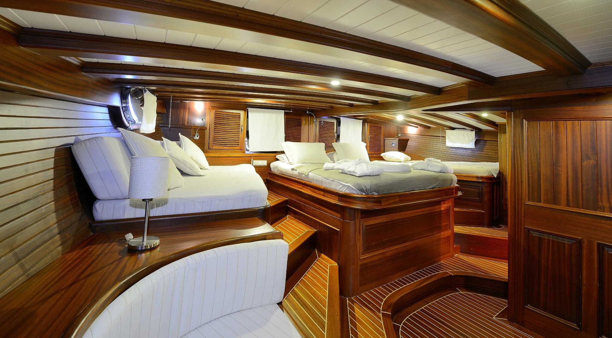 yacht cabin interior with double bed, white upholstered seating, and rich wood paneling