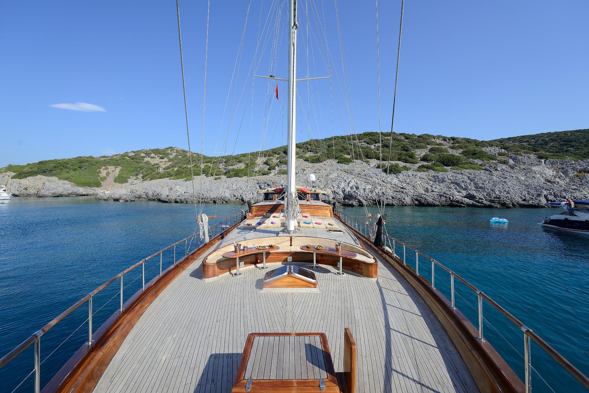 gulet bow deck featuring curved wooden seating area with white cushions and central mast